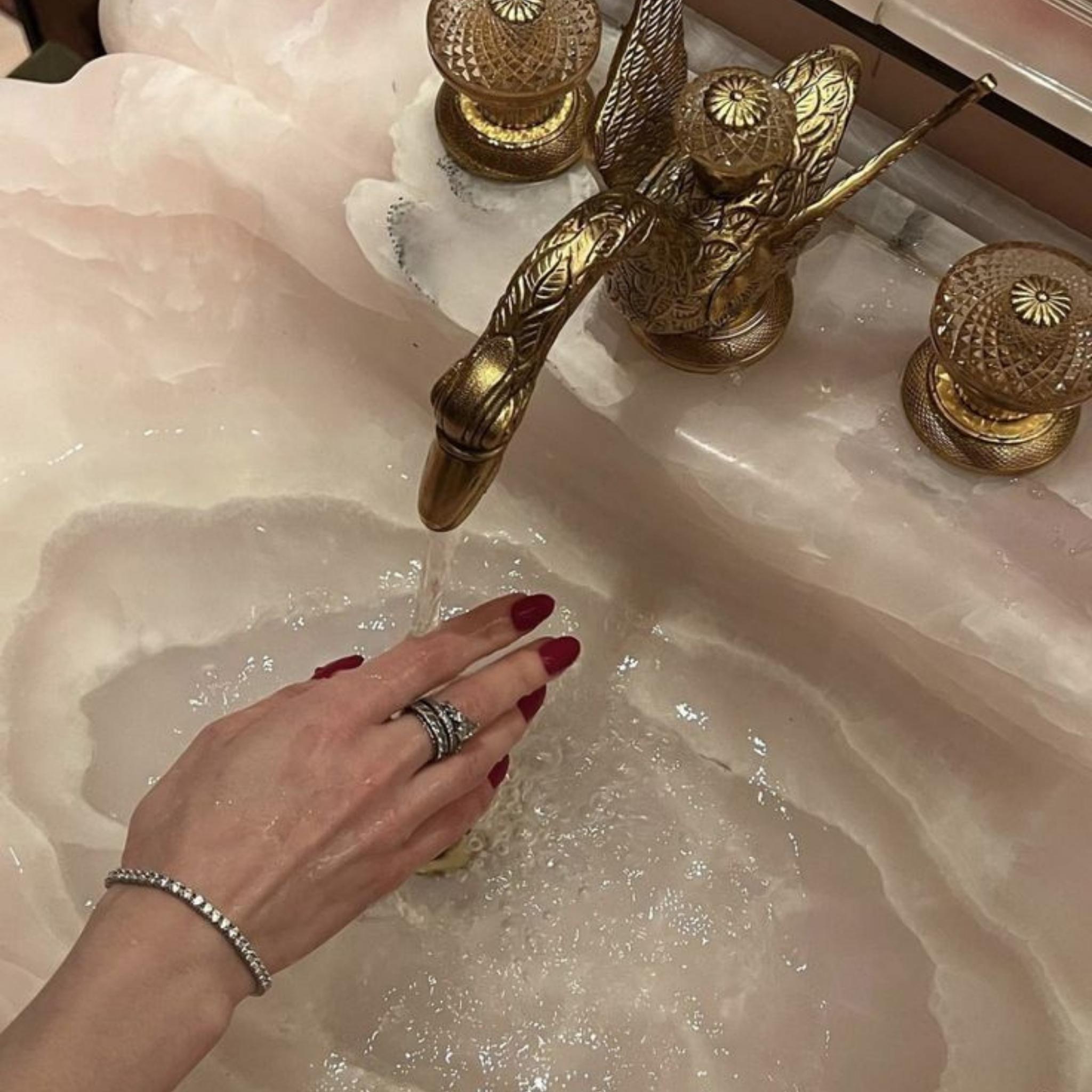 Hand in sink with water and gold taps, wearing rings