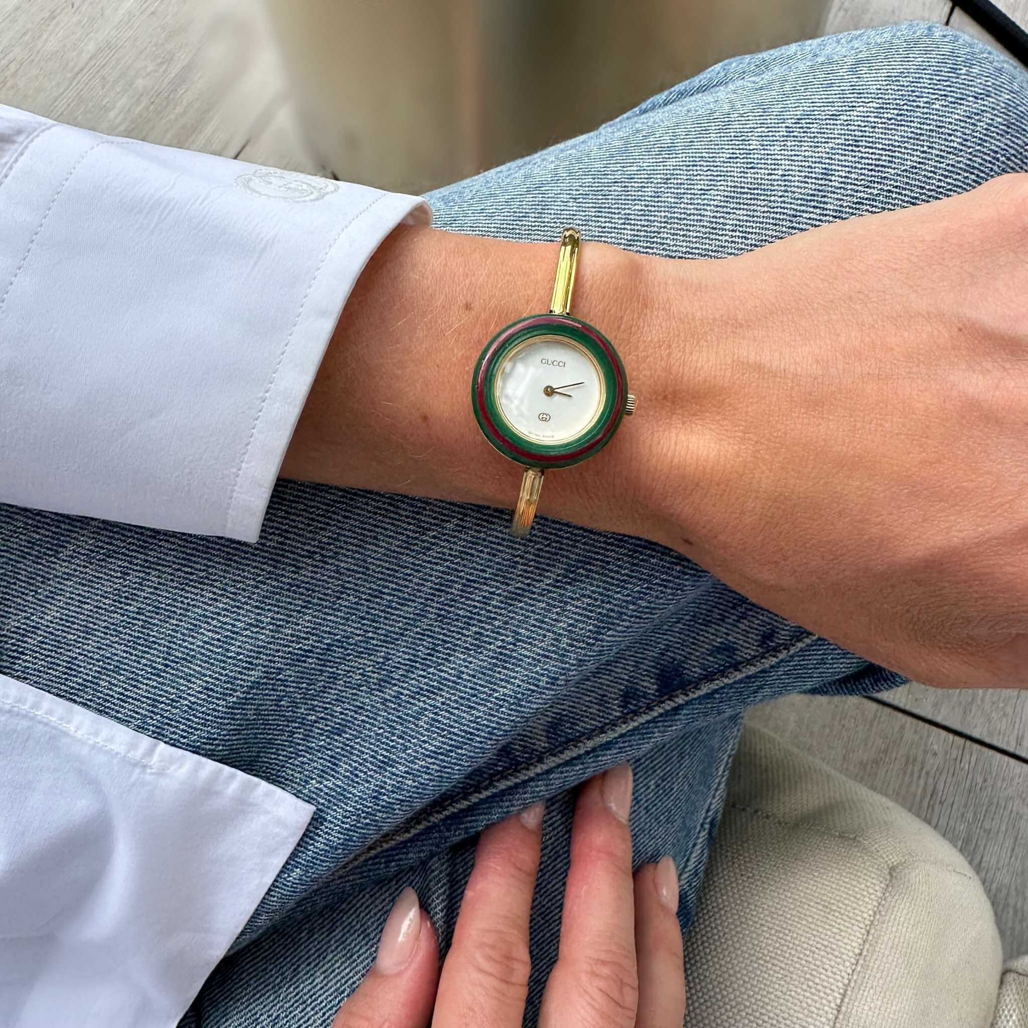 Person wearing a Gucci watch with a gold band on a casual setting