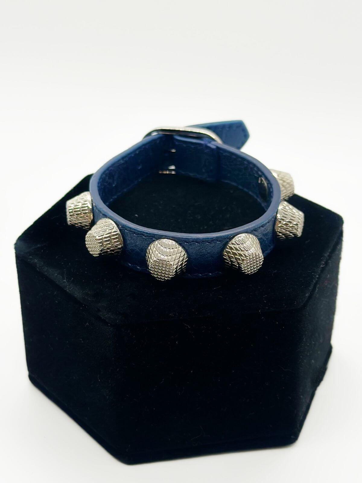 Balenciaga studded leather bracelet on black fixture on white background.