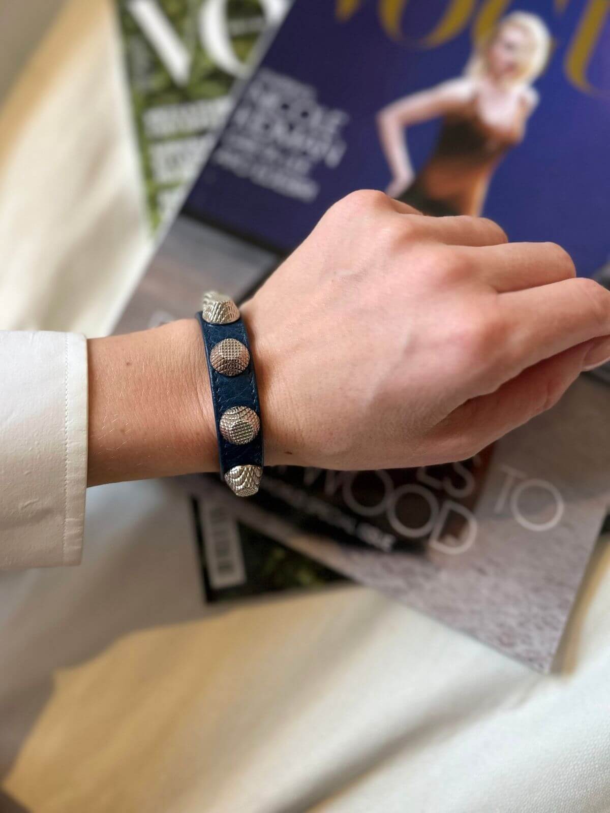 Hand wearing Balenciaga studded bracelet on a magazine background