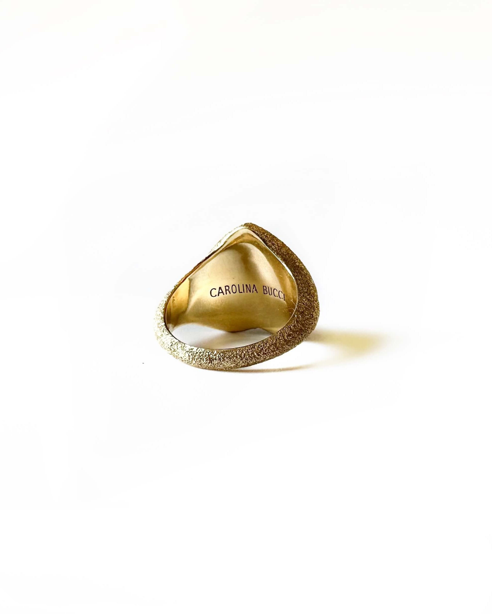 Carolina Bucci gold ring back side with signature engraving of name shown. The ring has a sparkle due to the texture. The ring is on a white background.