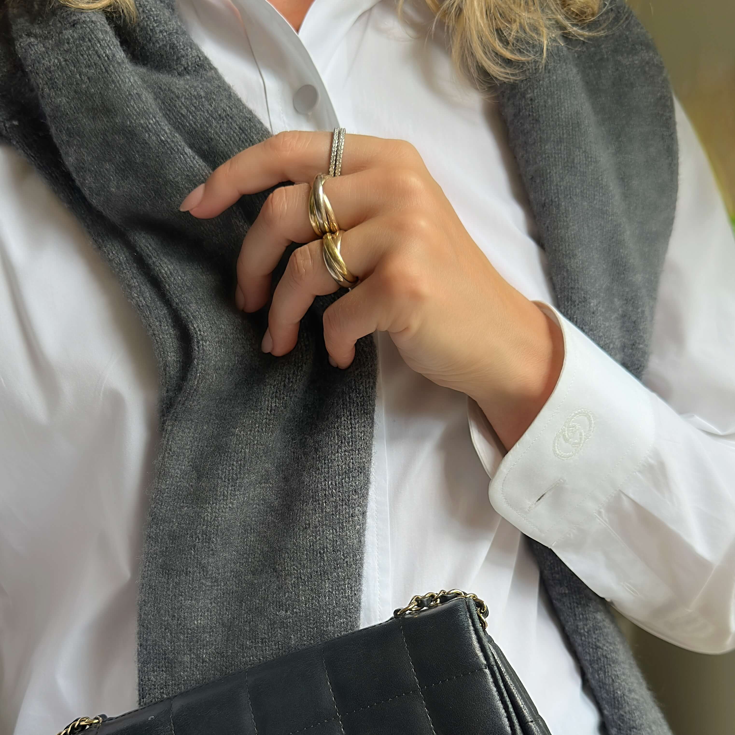 Person wearing a gray scarf and Cartier gold ring, holding a black handbag.