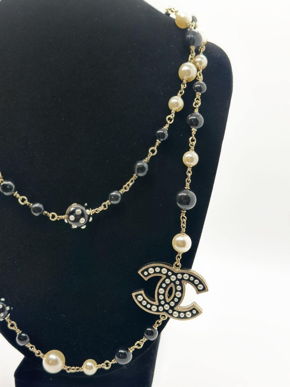 Chanel long bead and pearl necklace on black neckform on white background.
