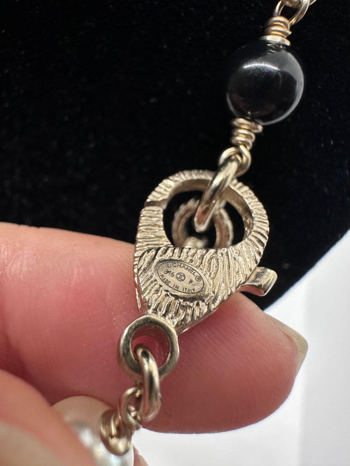 Chanel long bead and pearl necklace on black neckform on white background. Detail of signature.