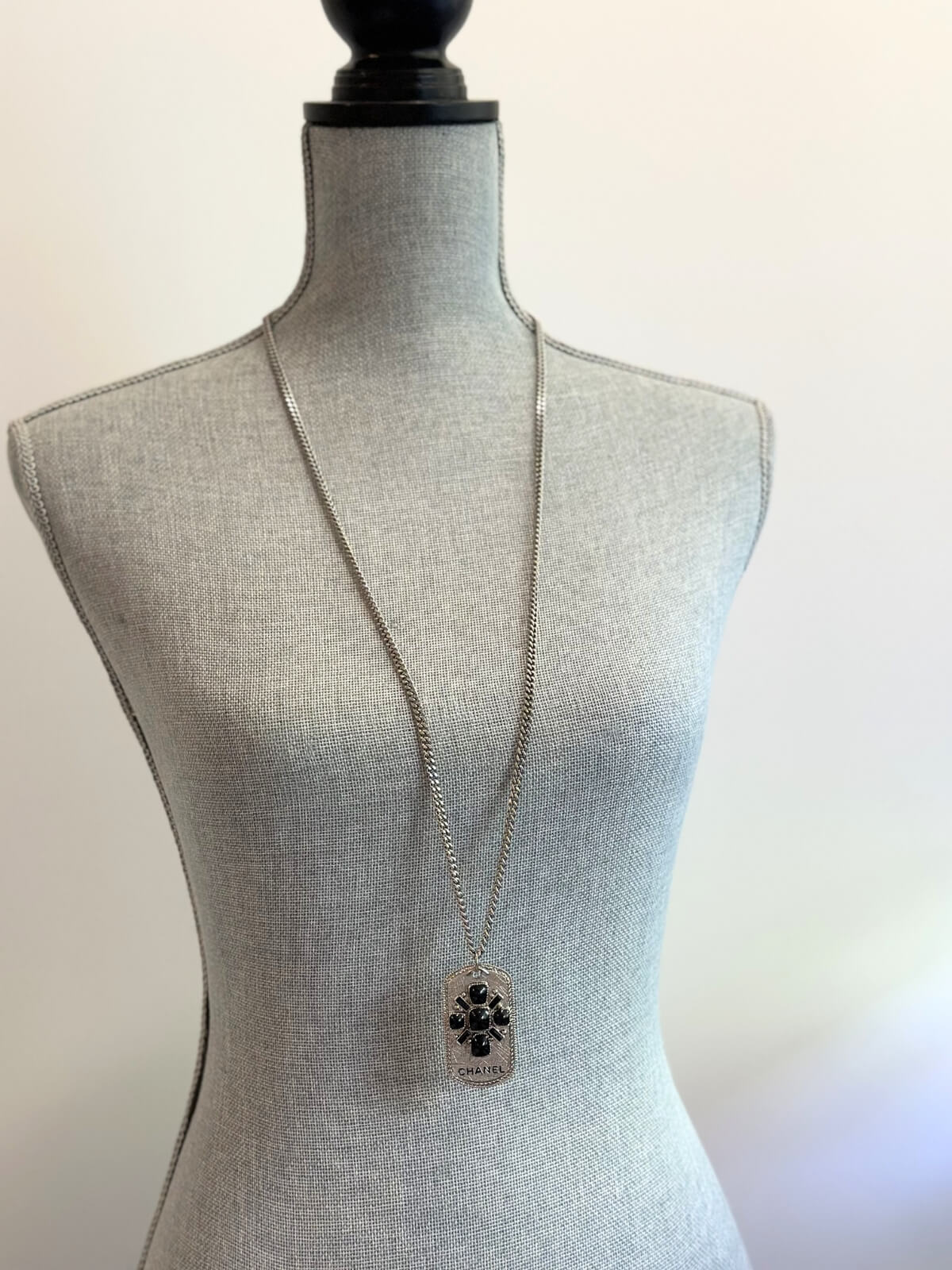 Louise Row Studio featuring Chanel long silver necklace with dog tag made with enamel design and CHANEL markings on body form.