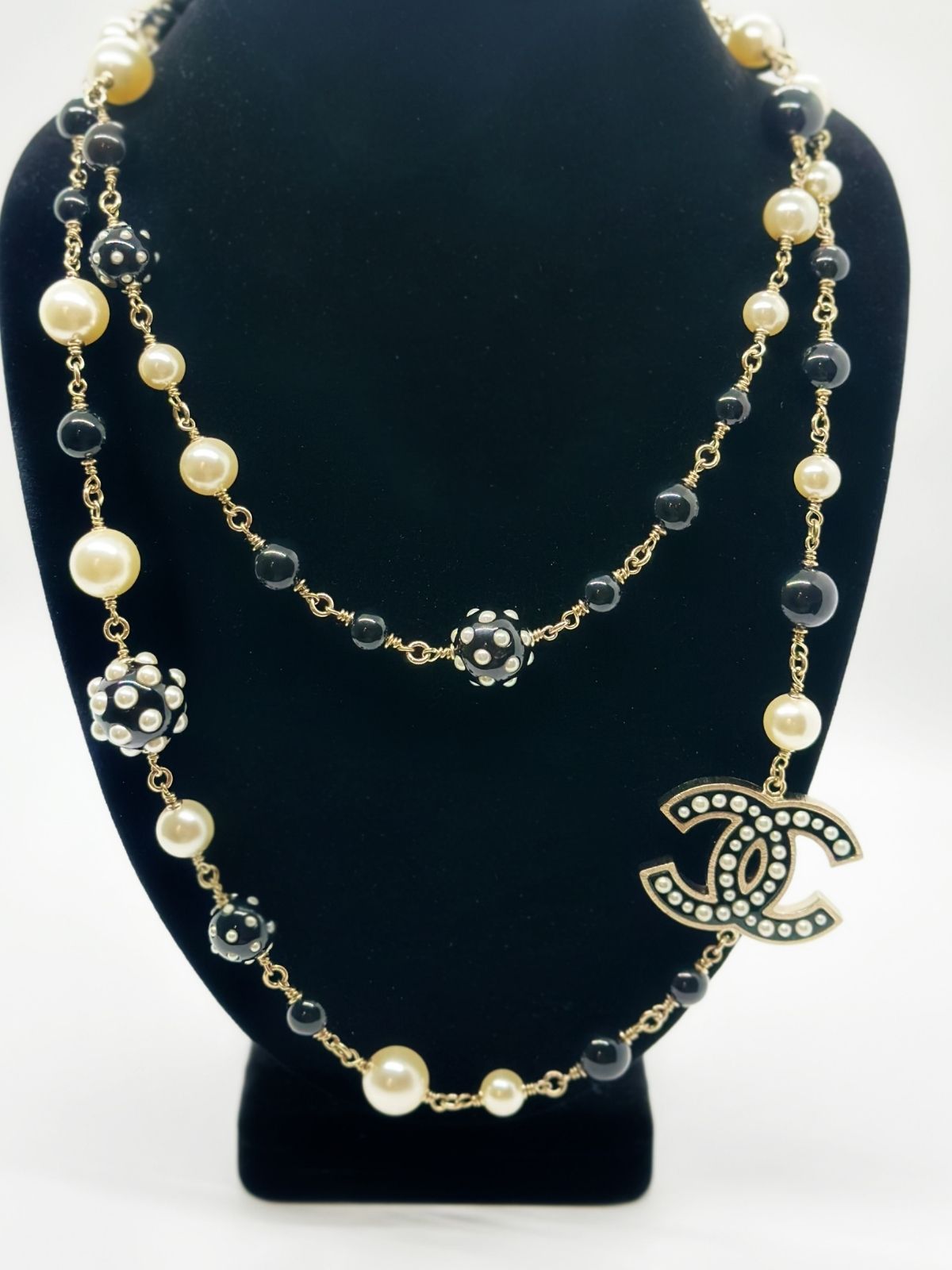 Chanel long bead and pearl necklace on black neckform on white background.