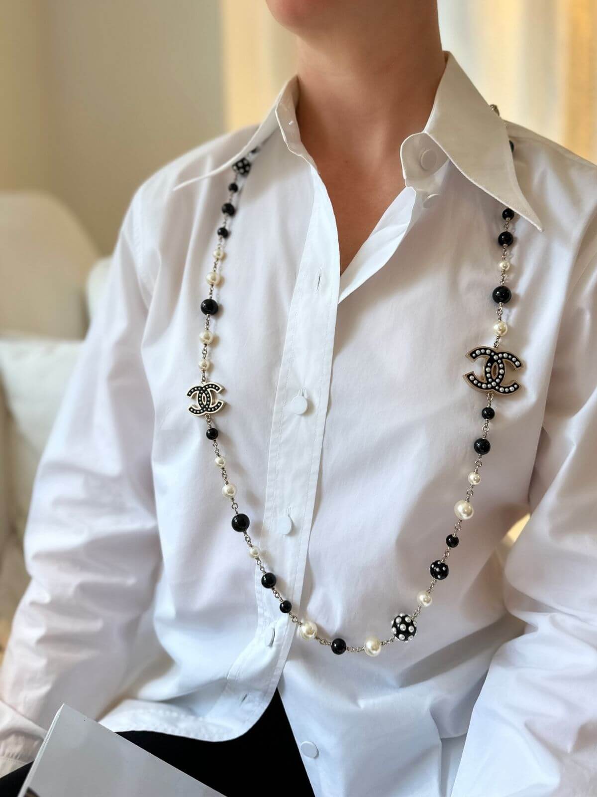Person wearing a Chanel necklace on a white shirt