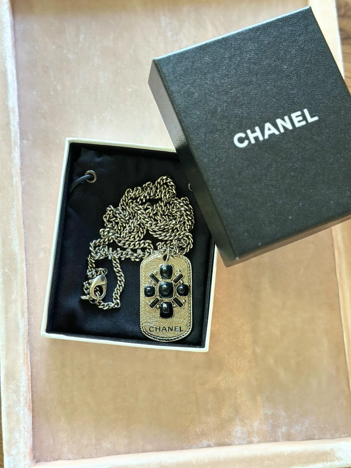 Louise Row Studio featuring Chanel long silver necklace with dog tag made with enamel design and CHANEL markings in Chanel box on pink pad.