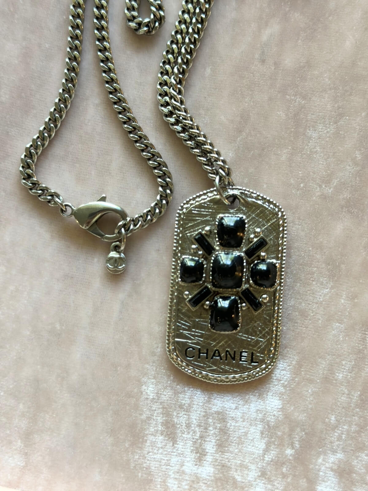 Louise Row Studio featuring Chanel long silver necklace with dog tag made with enamel design and CHANEL markings on pad showing stamp and detail.