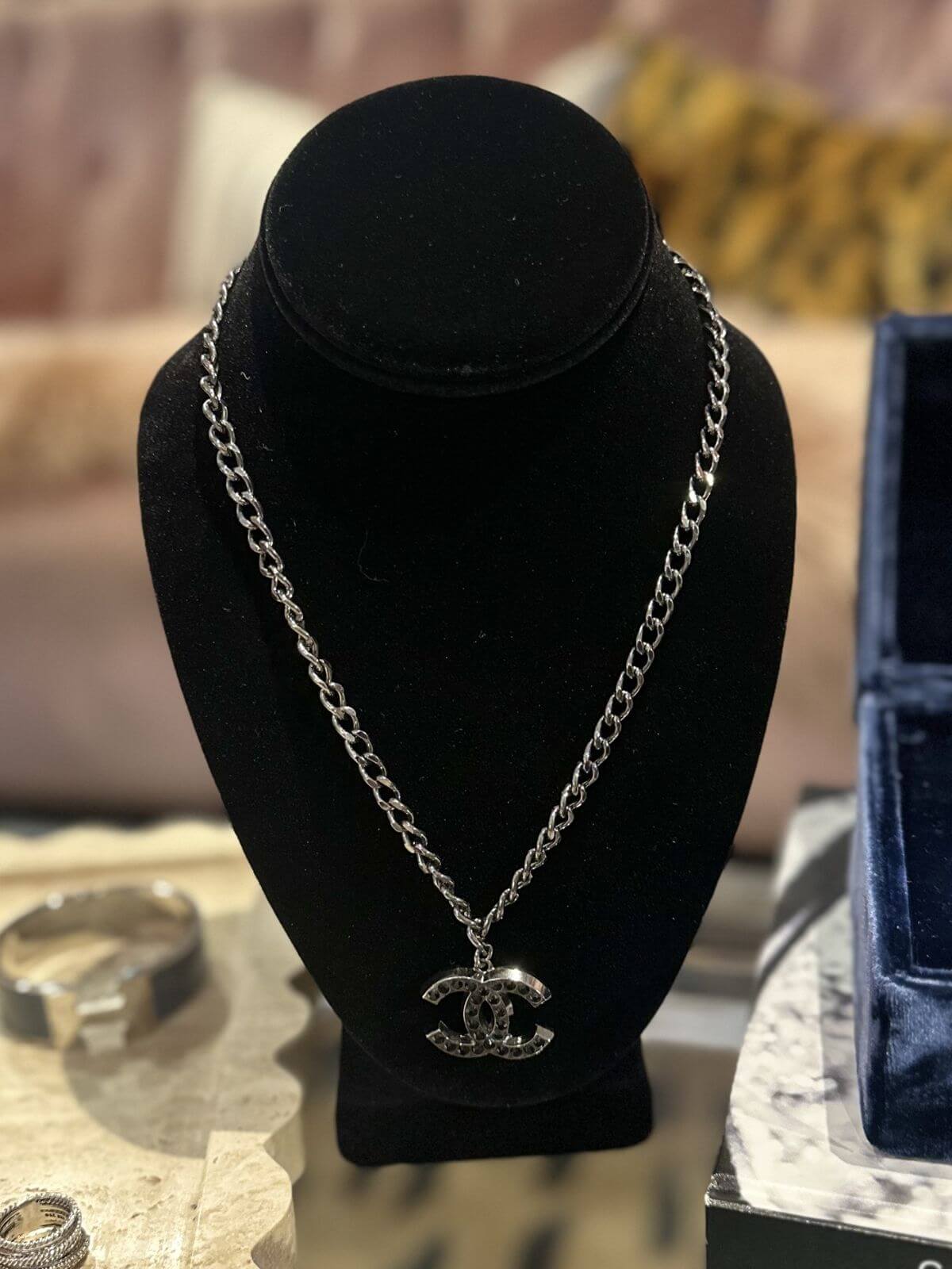Silver chain necklace with a CC logo on a black velvet stand.
