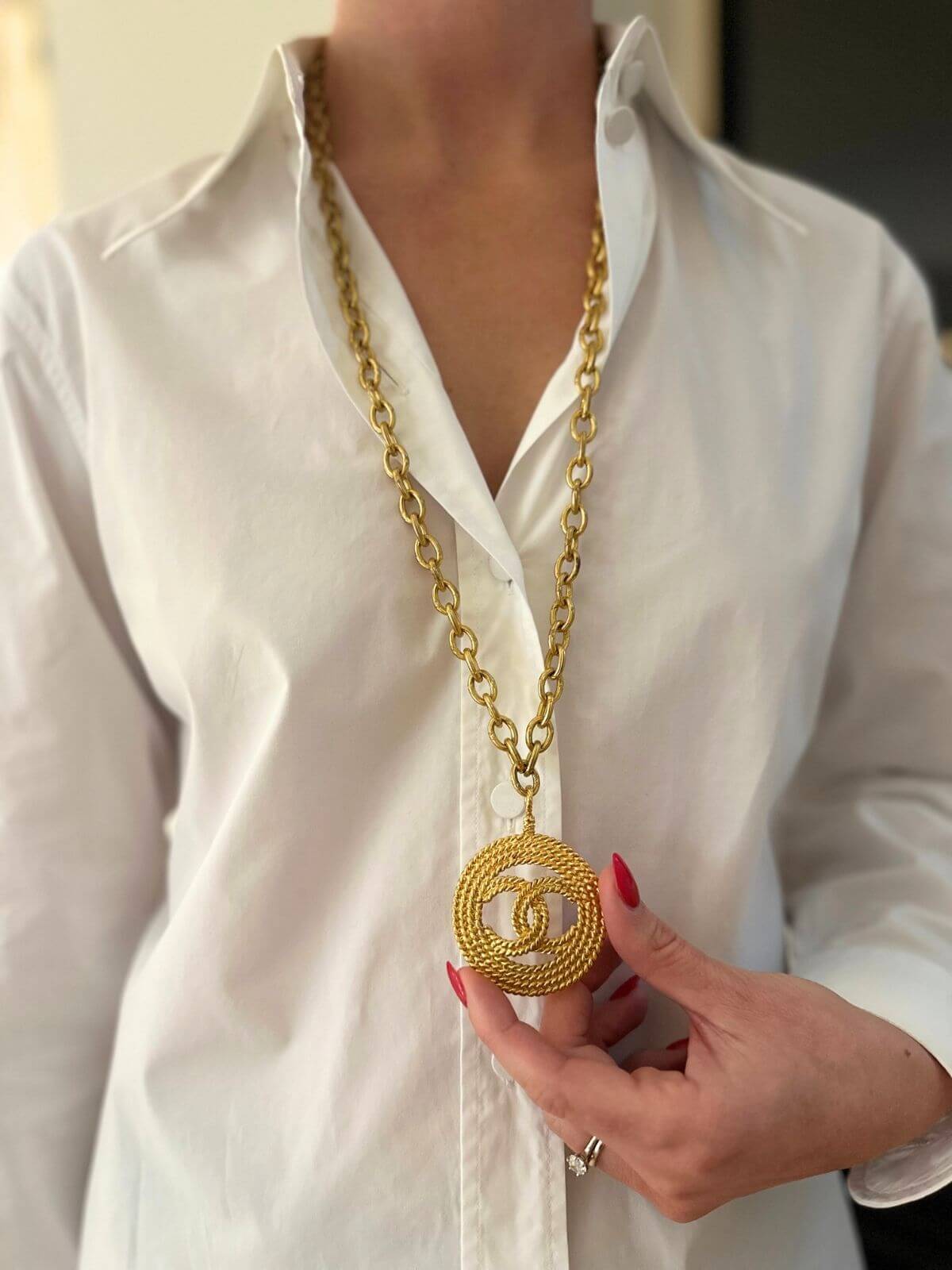 Louise Row Studio featuring Vintage Chanel medallion gold necklace on model with white shirt holding the necklace.