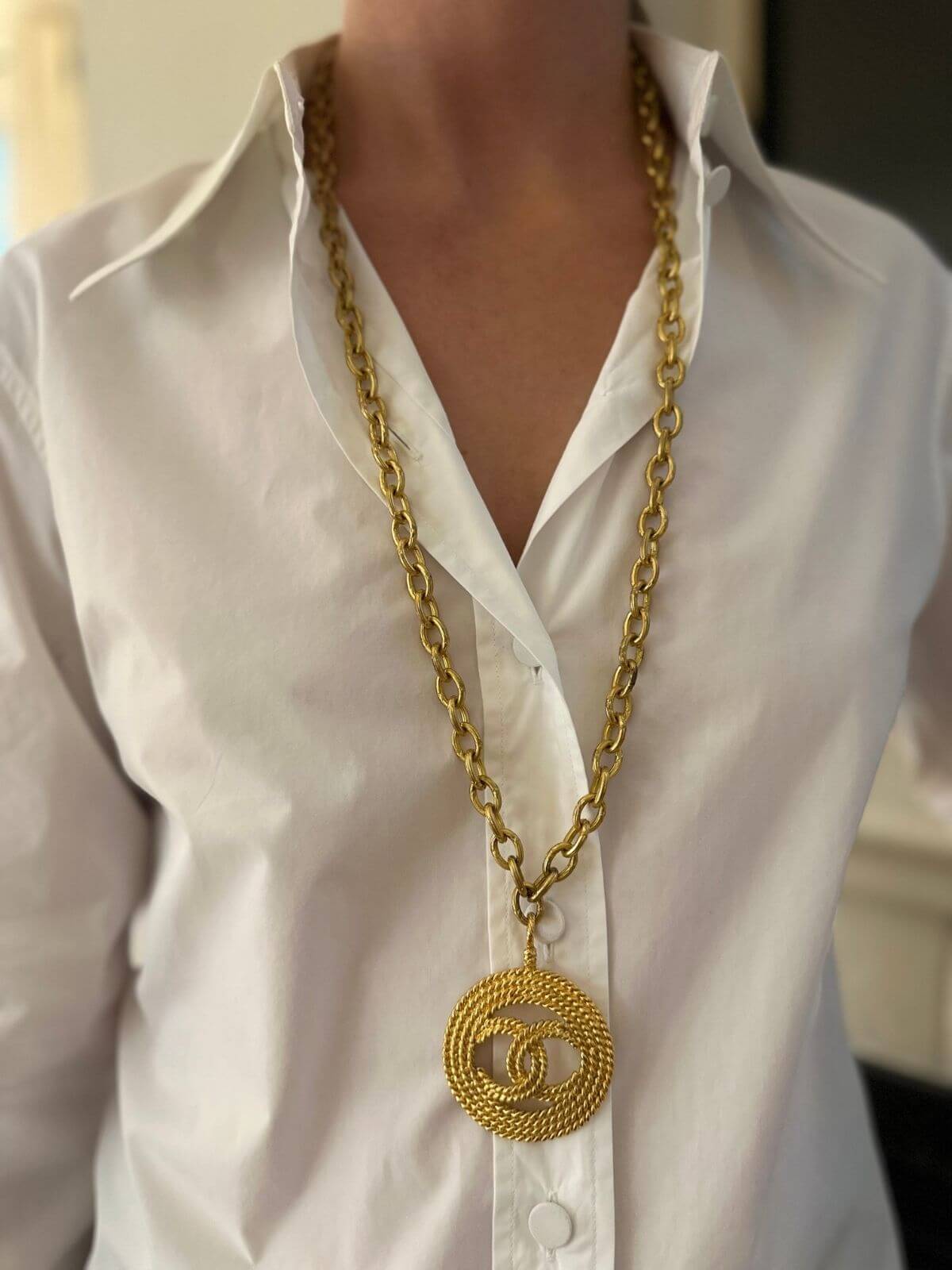 Gold chain necklace with a large circular pendant on a white shirt.