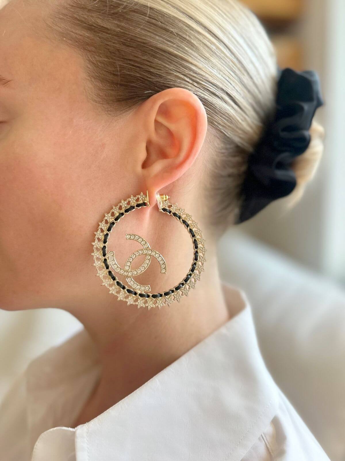 Close-up of a person wearing Chanel gold hoop earrings with a brand logo.
