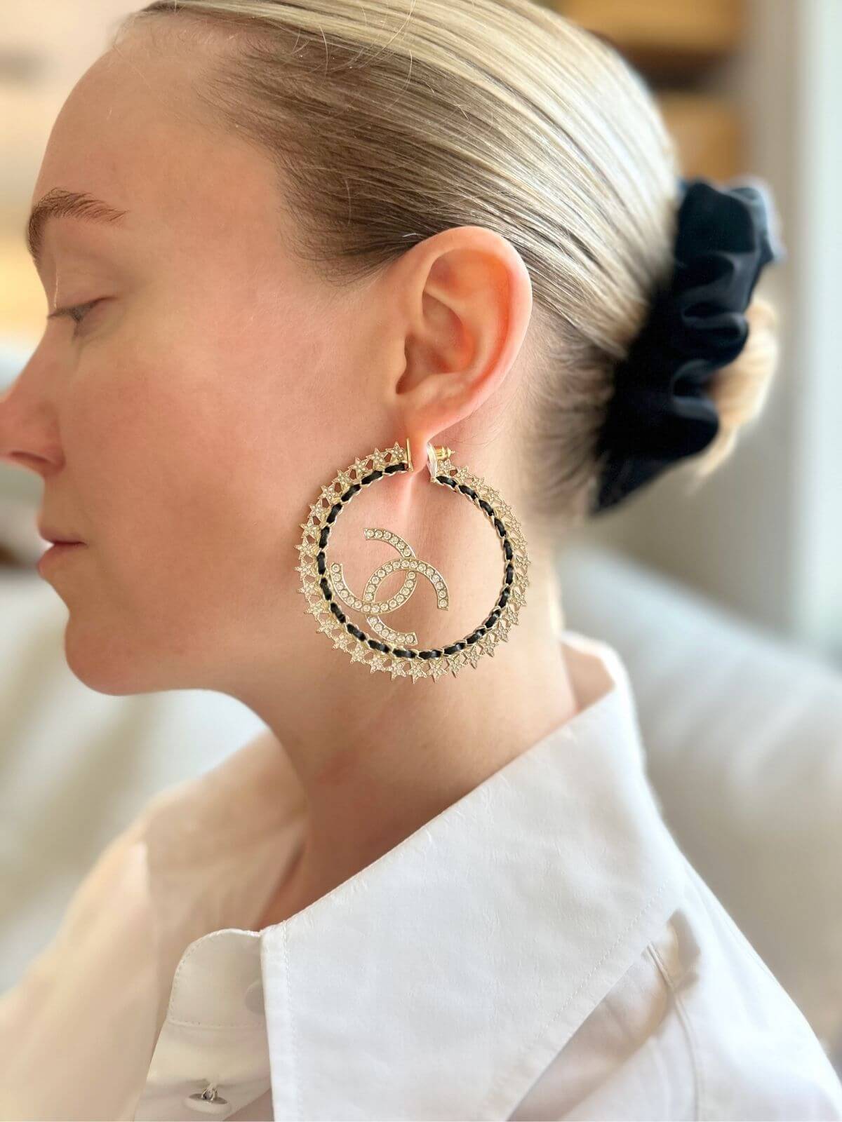 Close-up of a person wearing Chanel gold hoop earrings with a brand logo.
