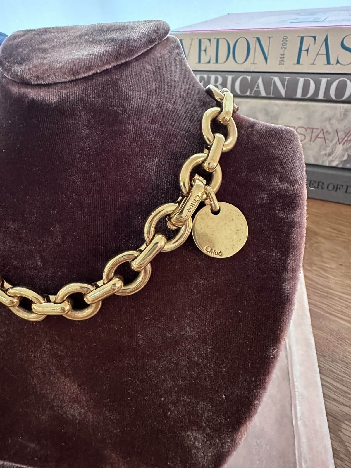 Gold chain necklace with a tag on a brown velvet stand, with a magazine in the background.