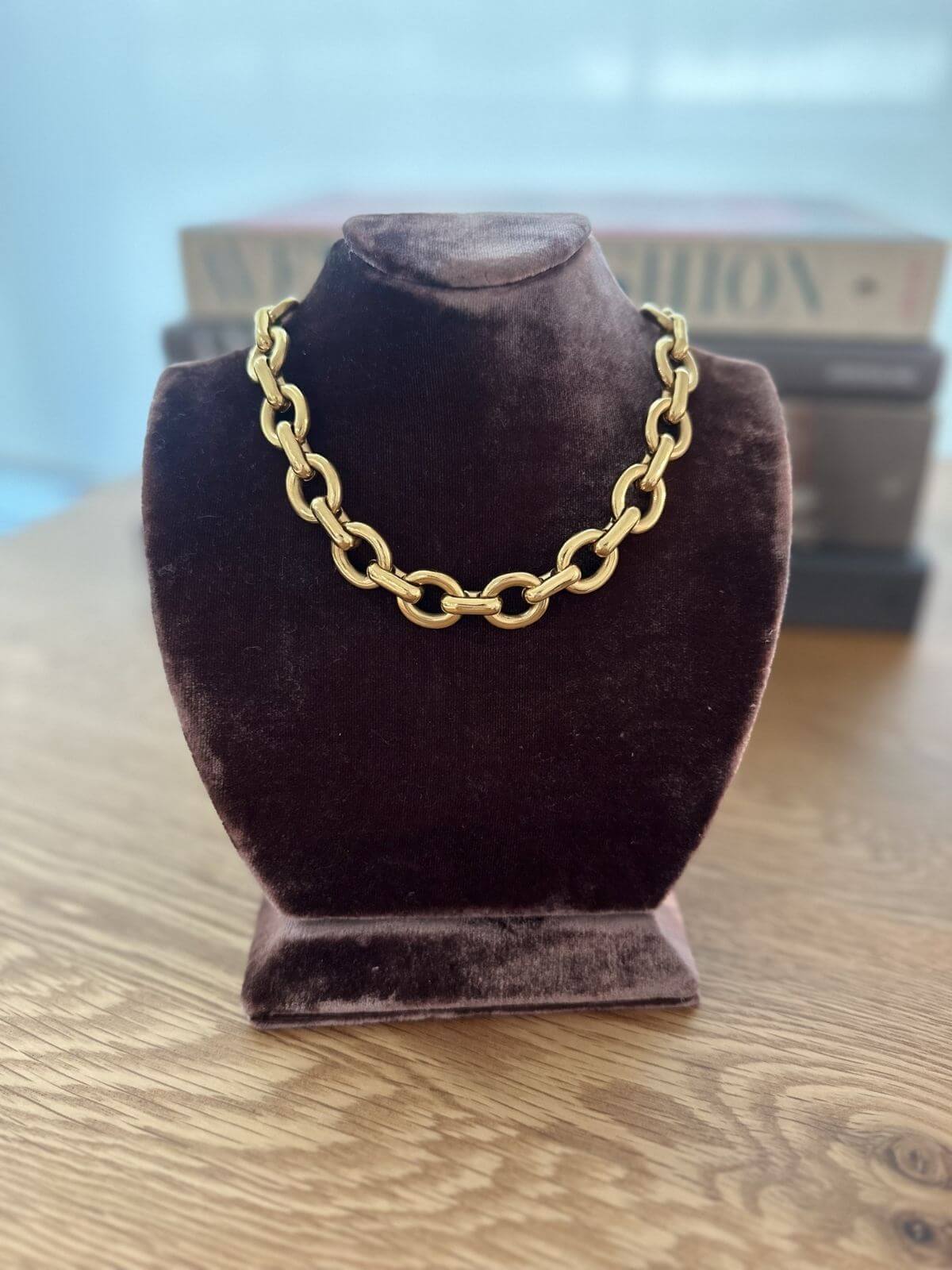 Gold chain necklace on a brown velvet bust against a blurred background