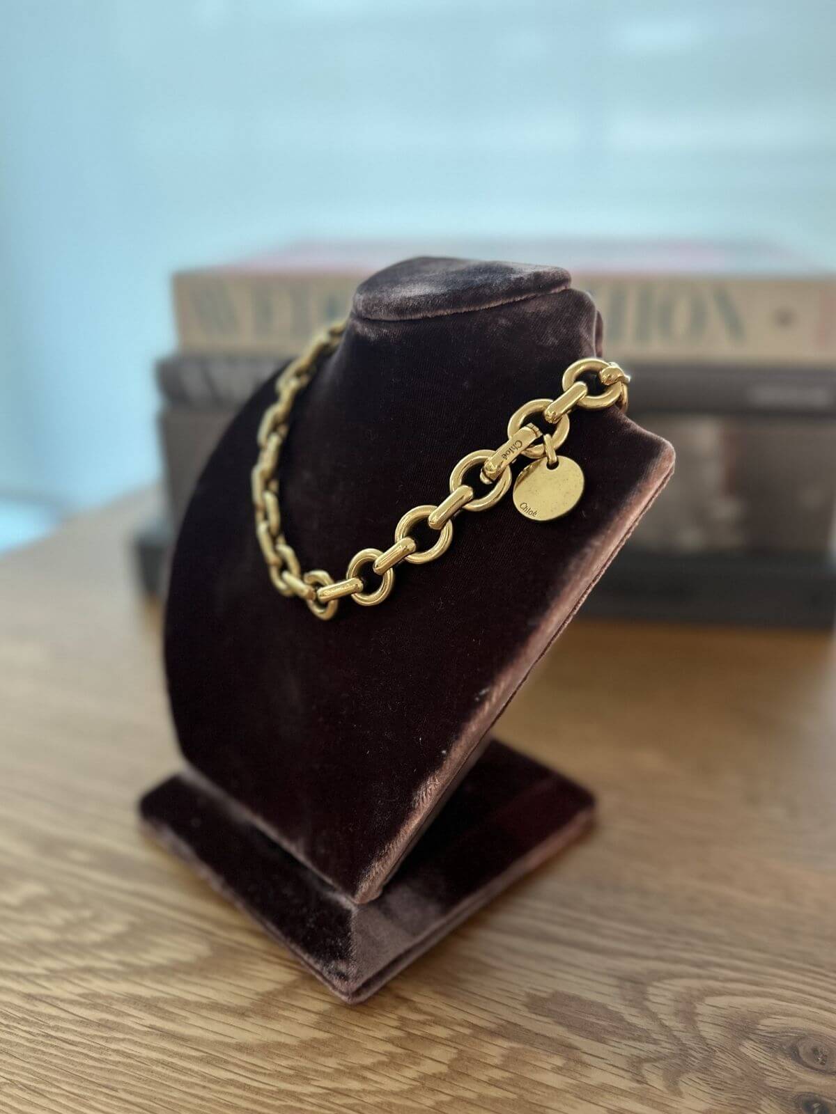 Gold chain necklace on a brown velvet stand with a blurred background