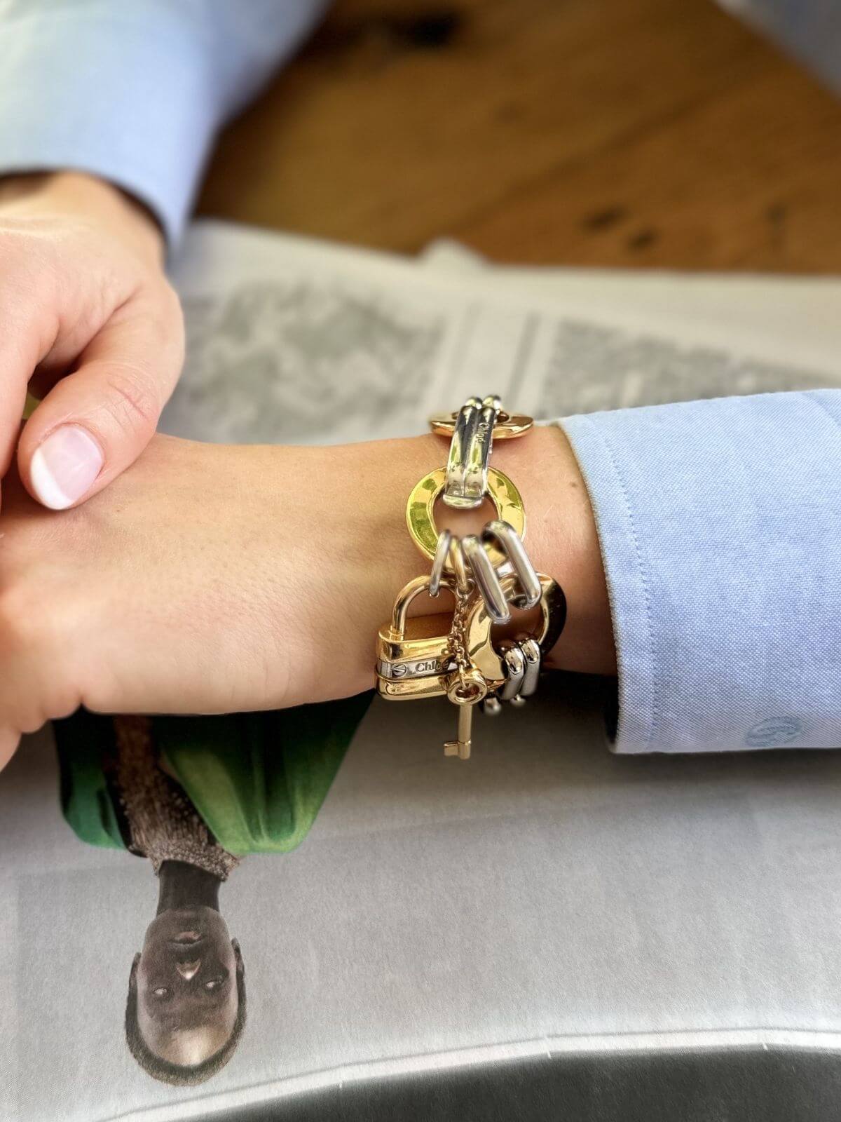 Close-up of a wrist wearing a gold charm bracelet on a wooden surface.