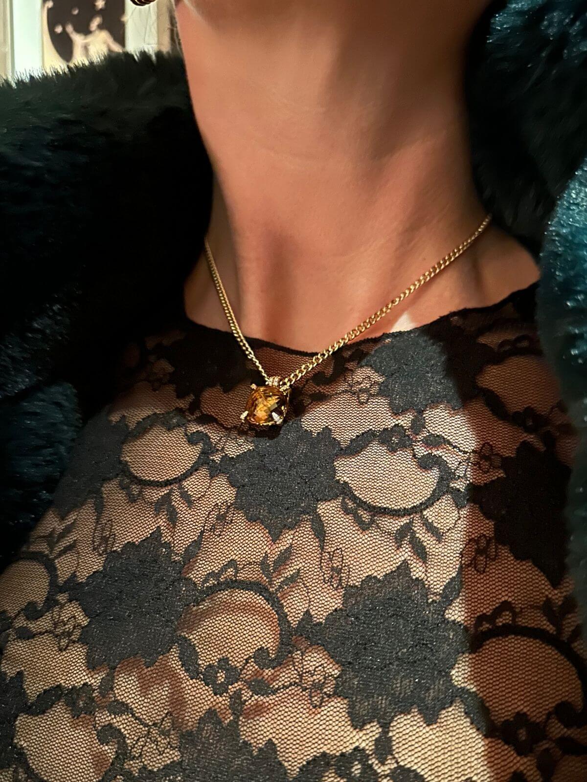 Person wearing a gold necklace with a pendant on a dark lace garment.