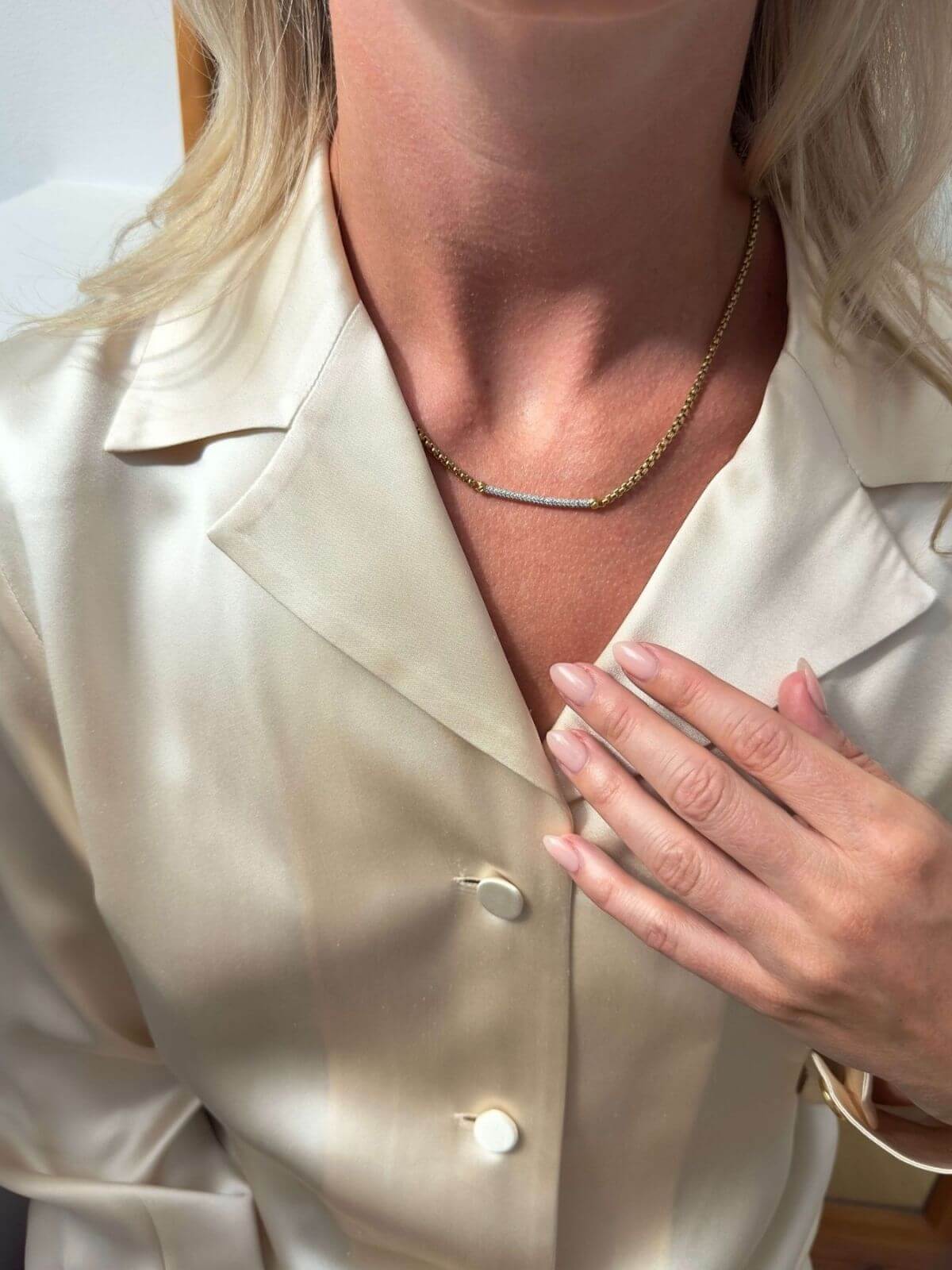 Model wearing silk shirt wearing gold DY bar necklace and touching her collar with manicured hand