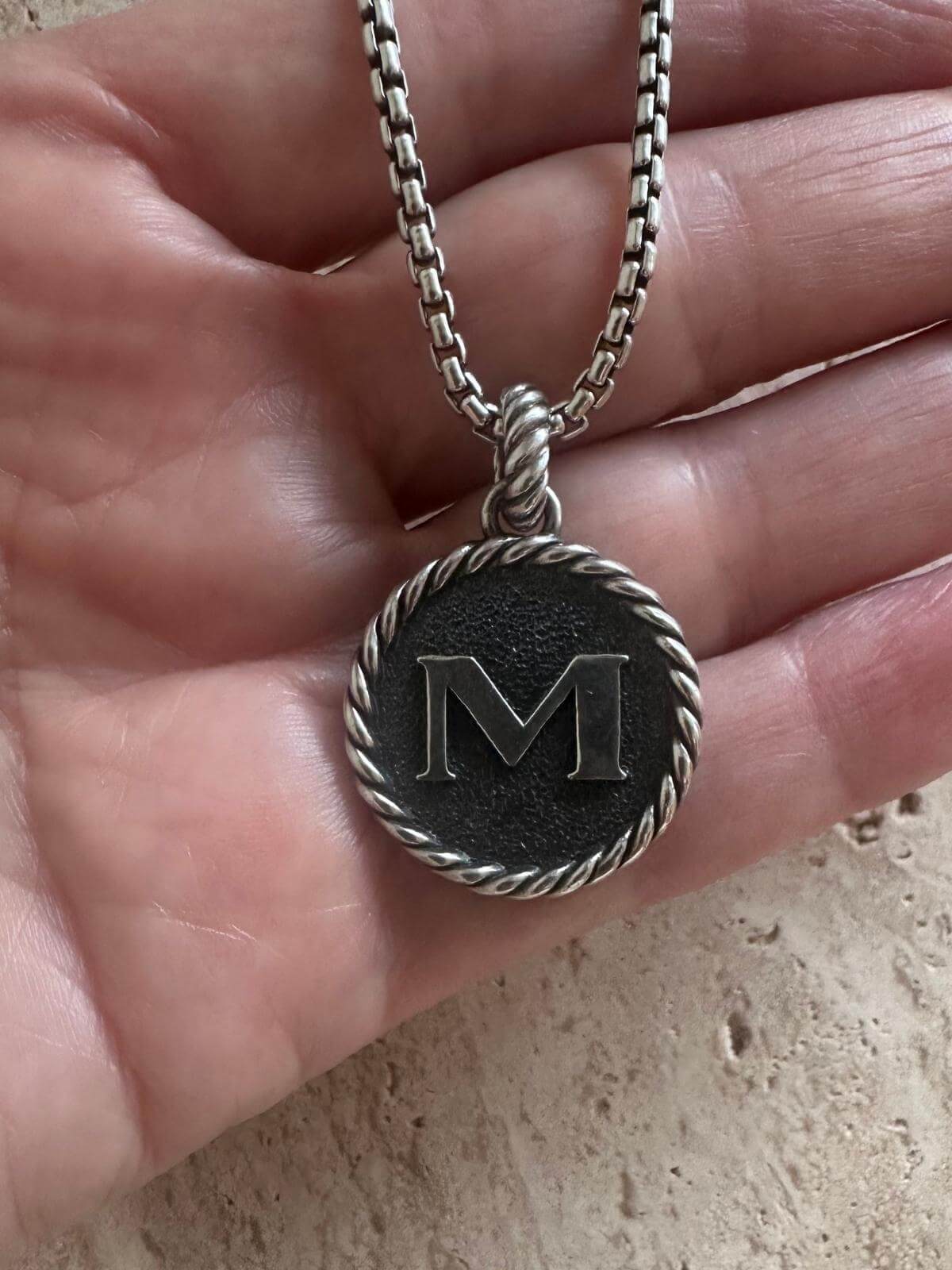 Hand holding DY silver pendant initial M on silver chain marble background