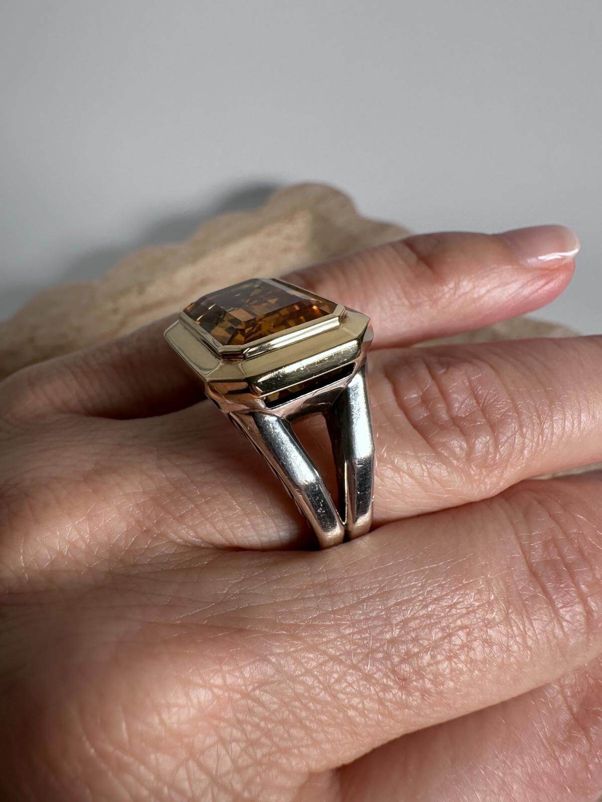 DY citrine and Gold ring with a large gemstone on a finger against a neutral background
