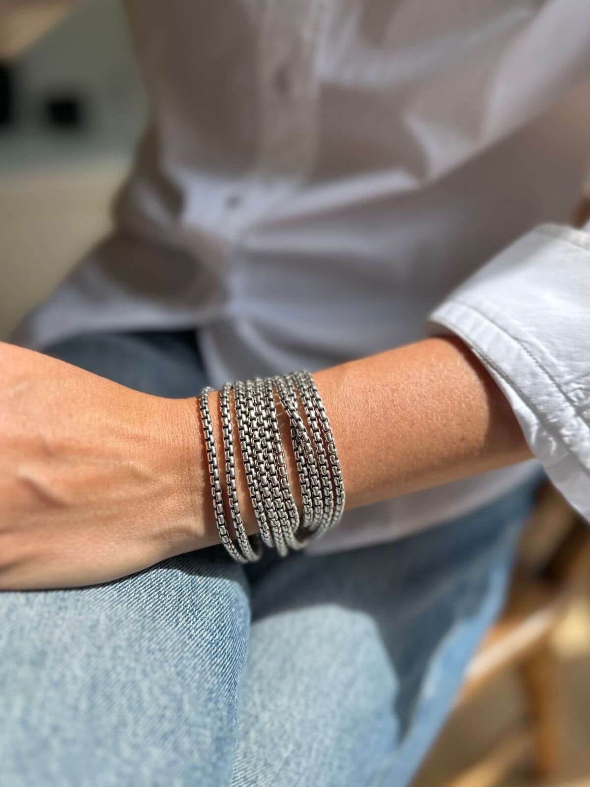 Model in white shirt wearing DY silver necklace wrapped as a bracelet around her wrist.