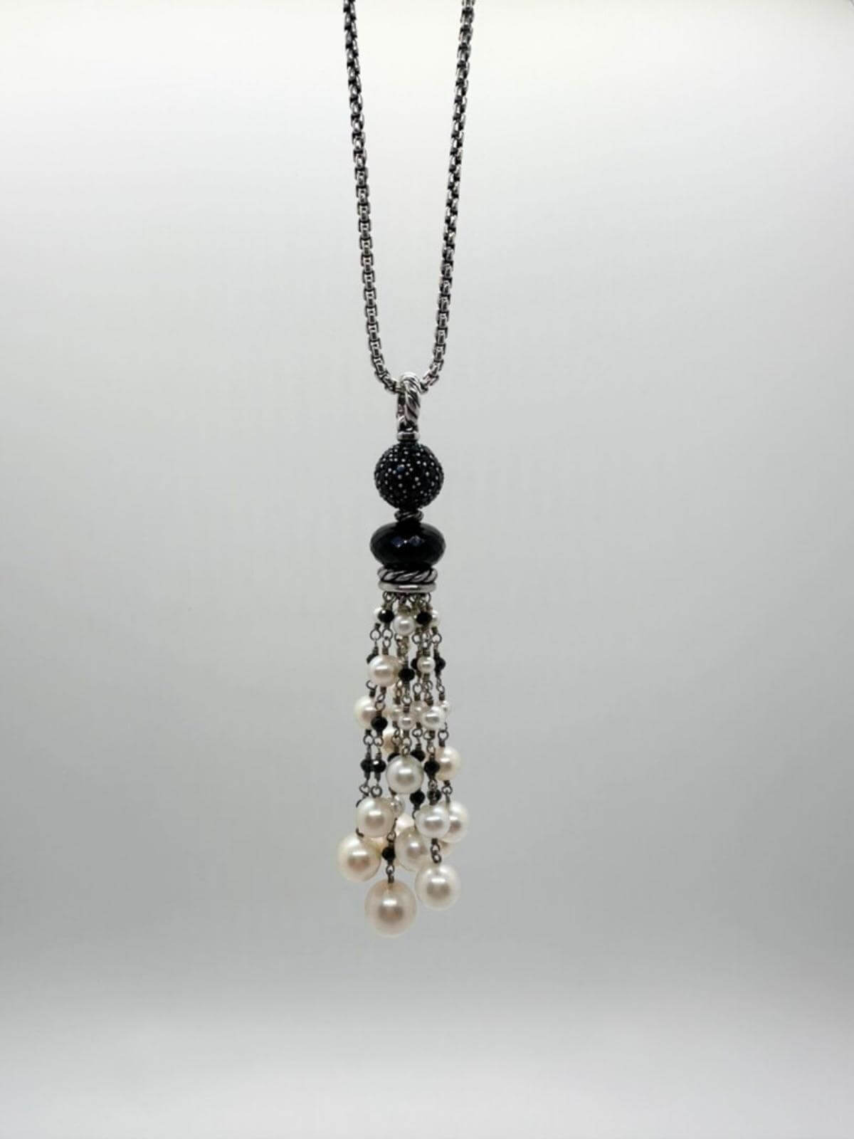 DY pendant with pearls and black onyx stones hanging on silver chain with white background.