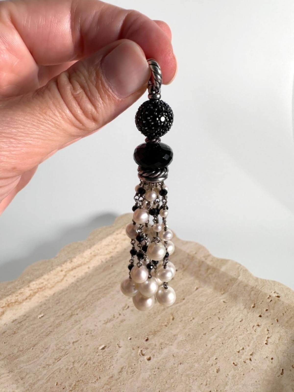 hand holding Pearl beads and onyx pendant set in silver on marble background