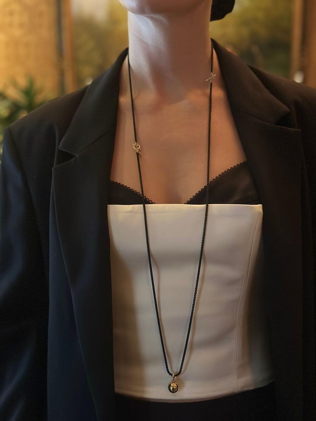 Person wearing a black blazer with a white pouch and gold necklace.