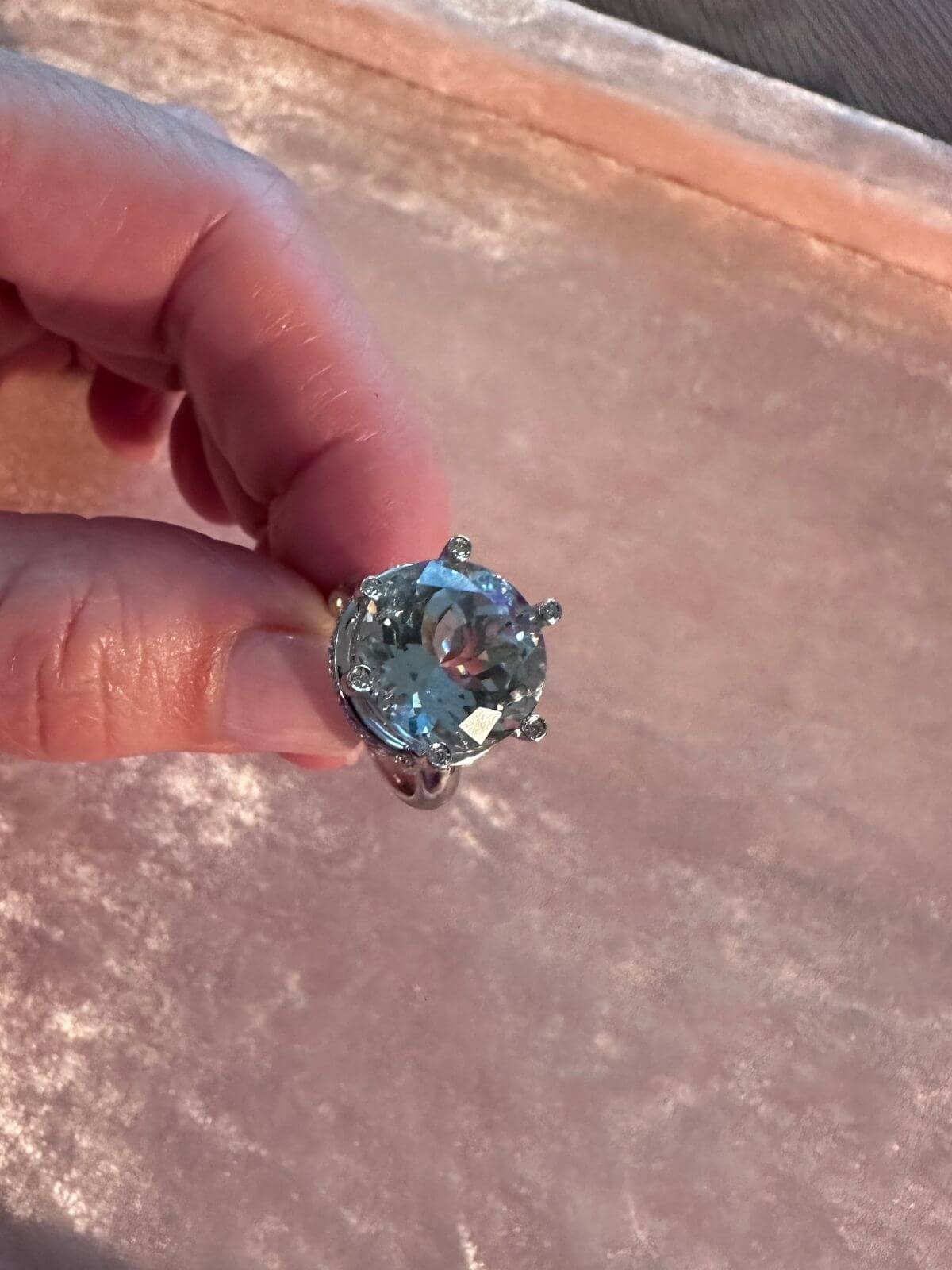 Ring with a large blue gemstone held in a hand against a pinkish background