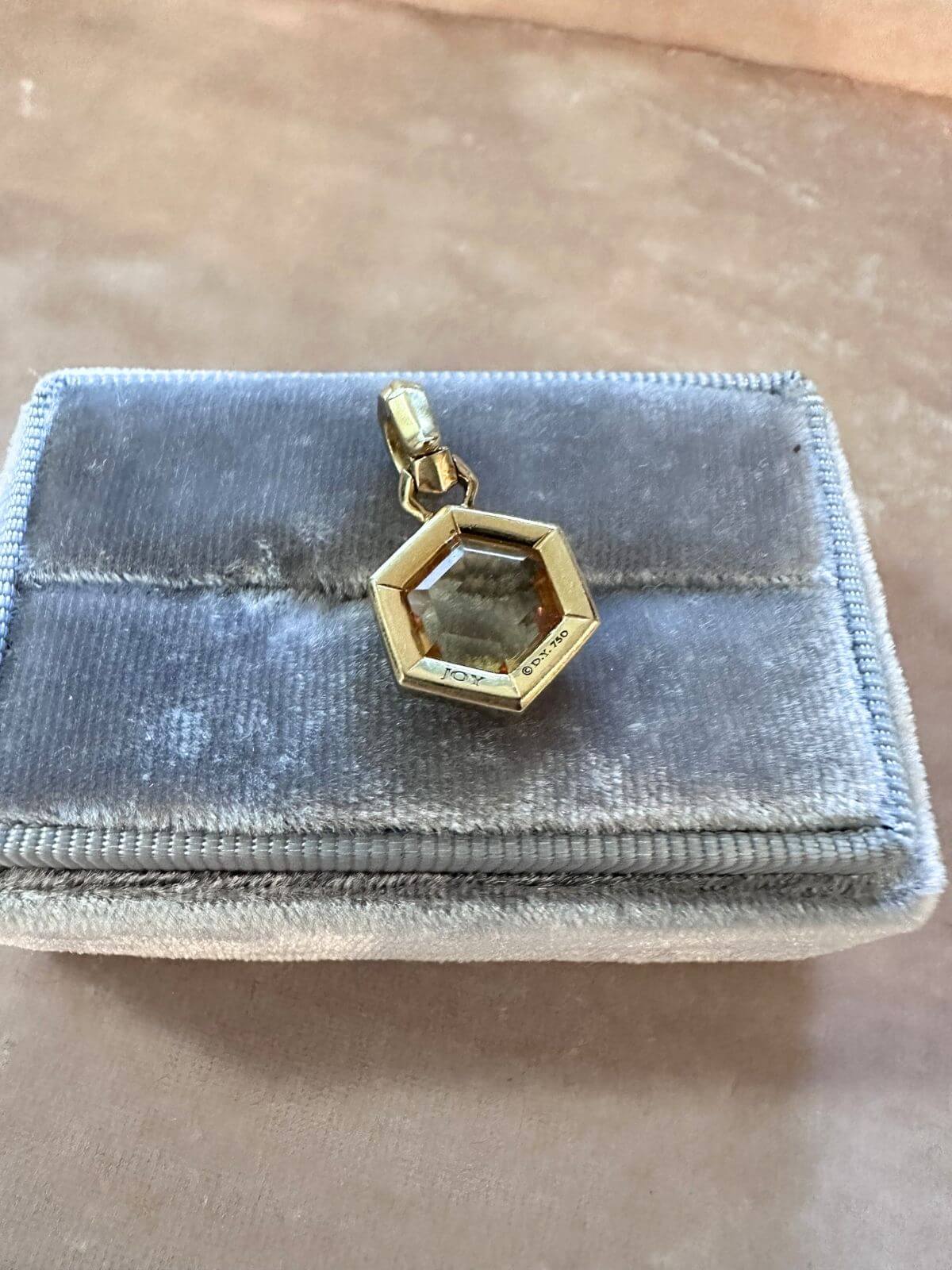 David Yurman Gold necklace with a hexagonal pendant on a pink fixture showing signature on back