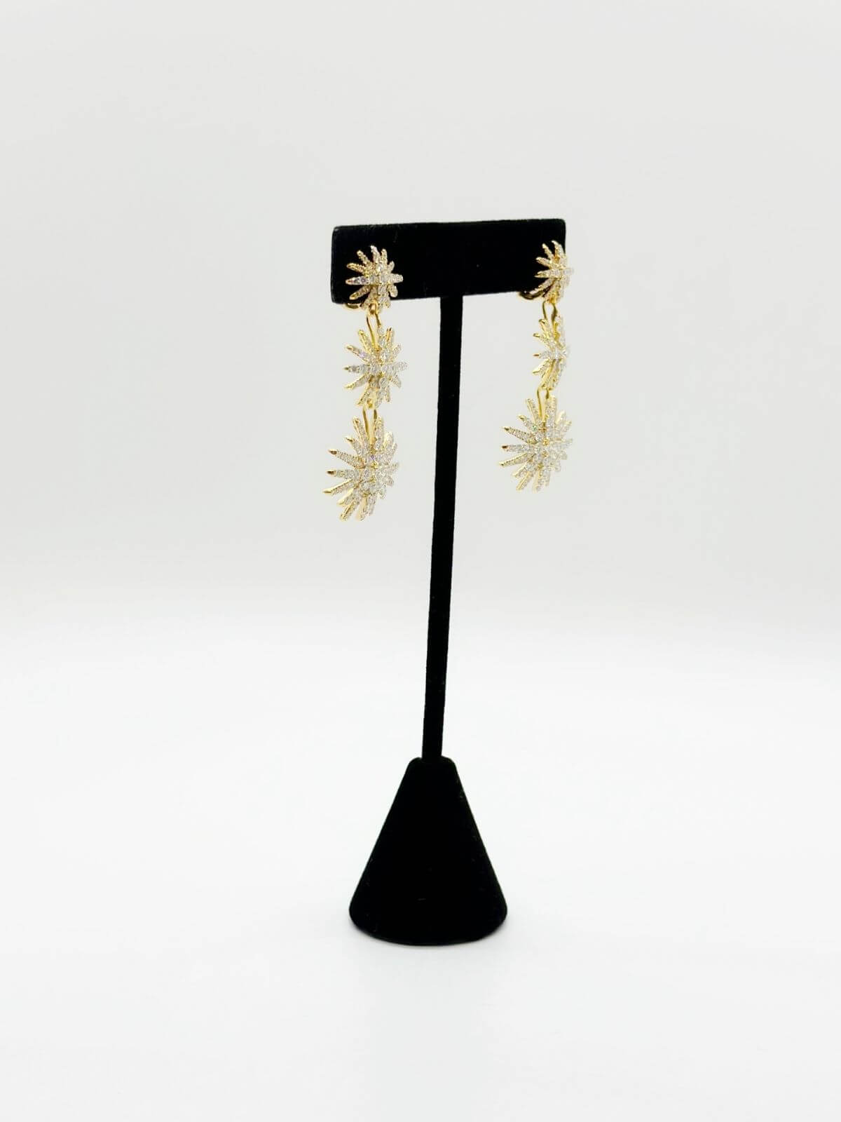 Gold floral earrings on a black stand against a white background
