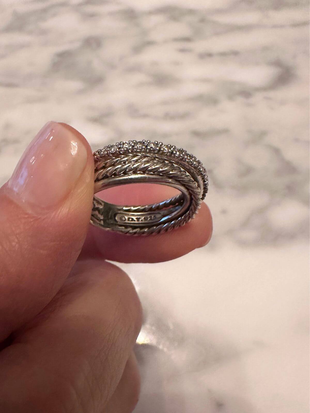 David Yurman crossover silver ring showing signature on the back , held by fingers.