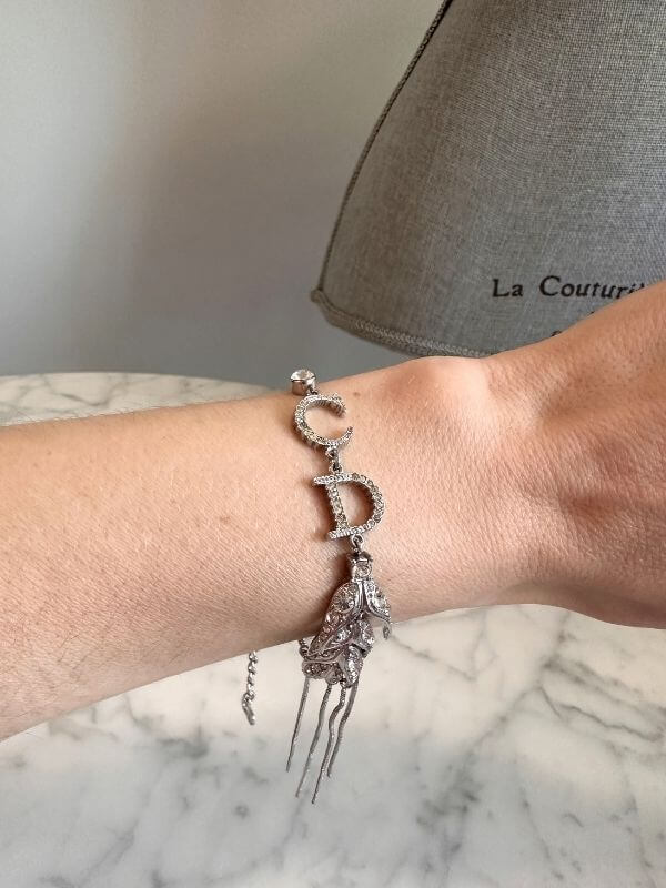 Louise Row Studio featuring Dior silver feather inspired bracelet made of silver and crystals on arm with marble table below.