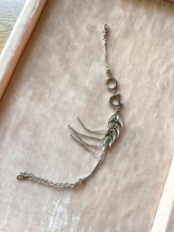 Louise Row Studio featuring Dior silver feather inspired bracelet made of silver and crystals on pink pad showing backside.