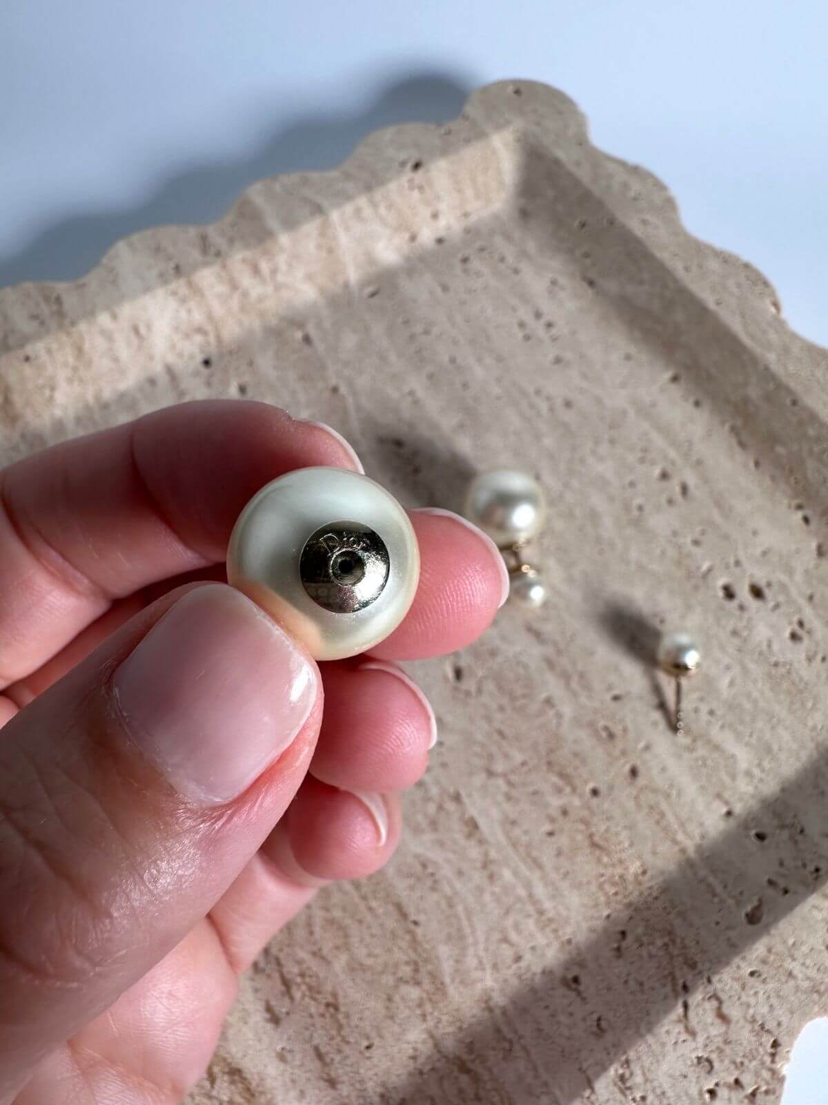 Hand holding a pearl earring showing back signature with a textured surface in the background
