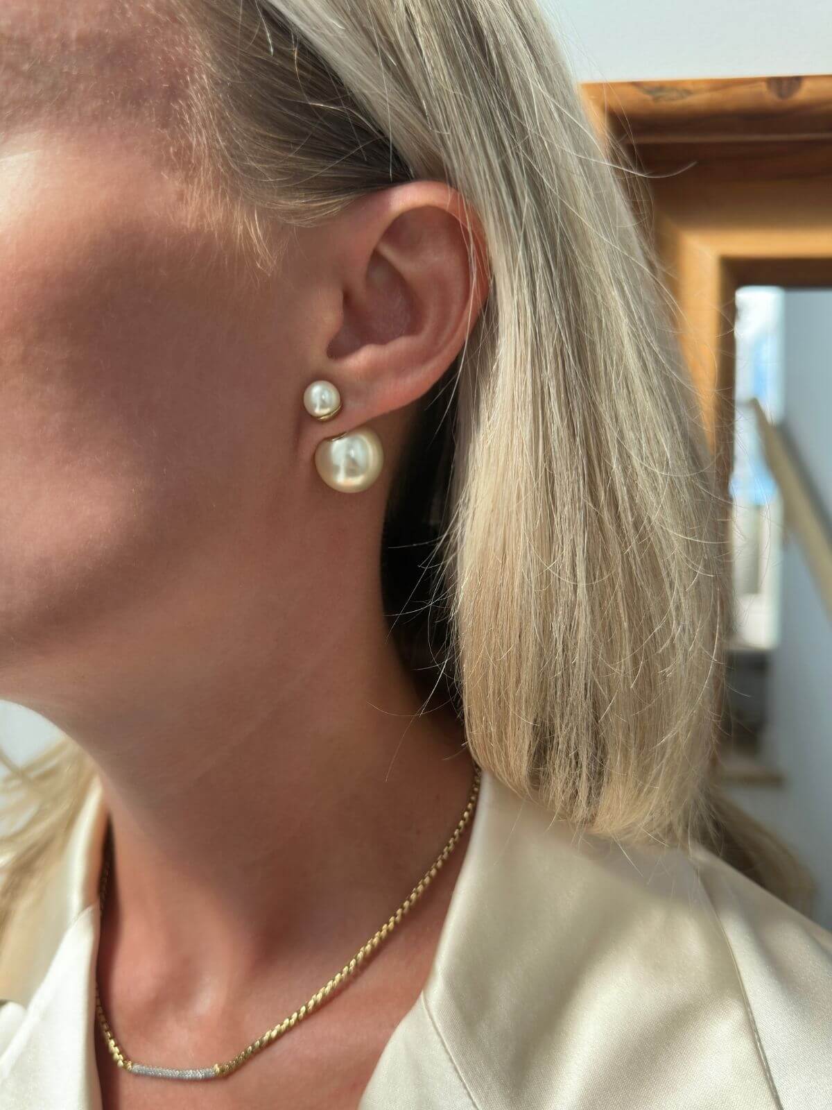 Close-up of a person wearing pearl earrings with a neutral background