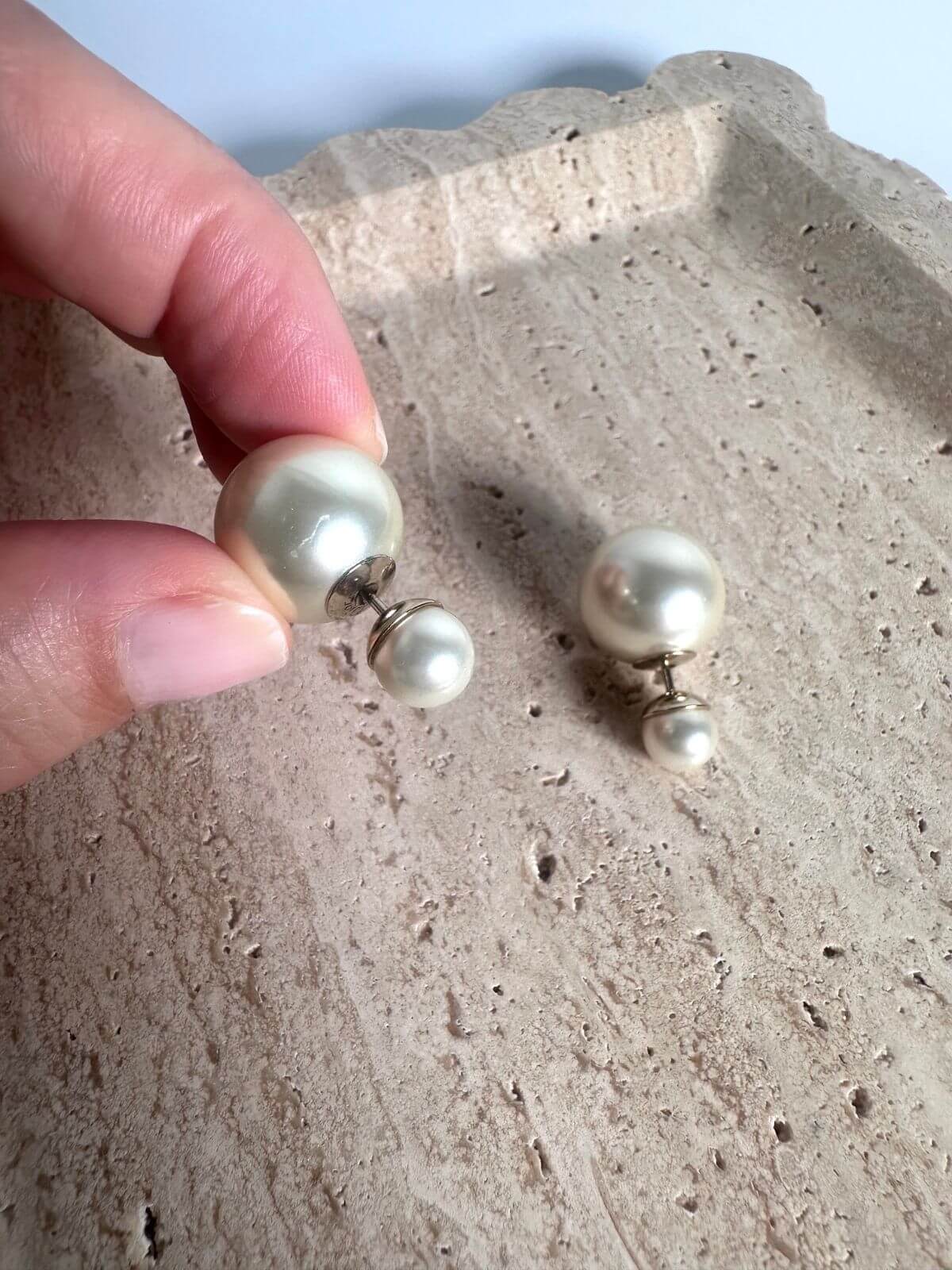 Pearl Dior earrings held by a hand on a textured surface