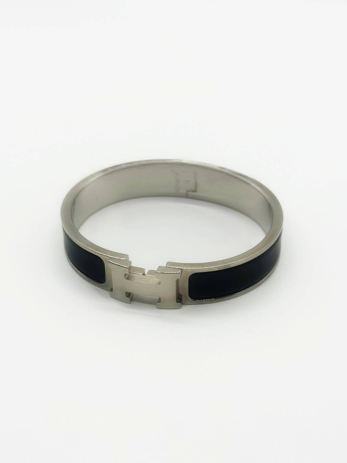 Hermes Clic H bracelet in stainless steel and black enamel on white background.