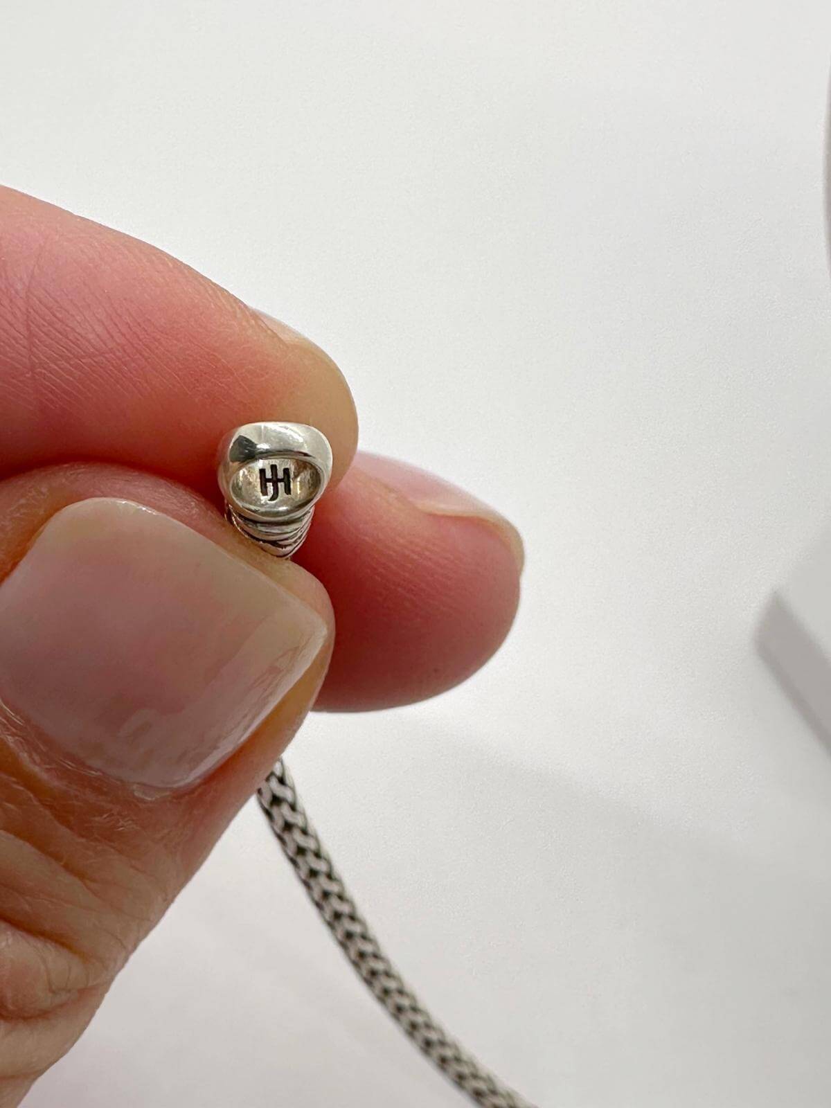 hand showing John Hardy stamp on silver necklace and white background