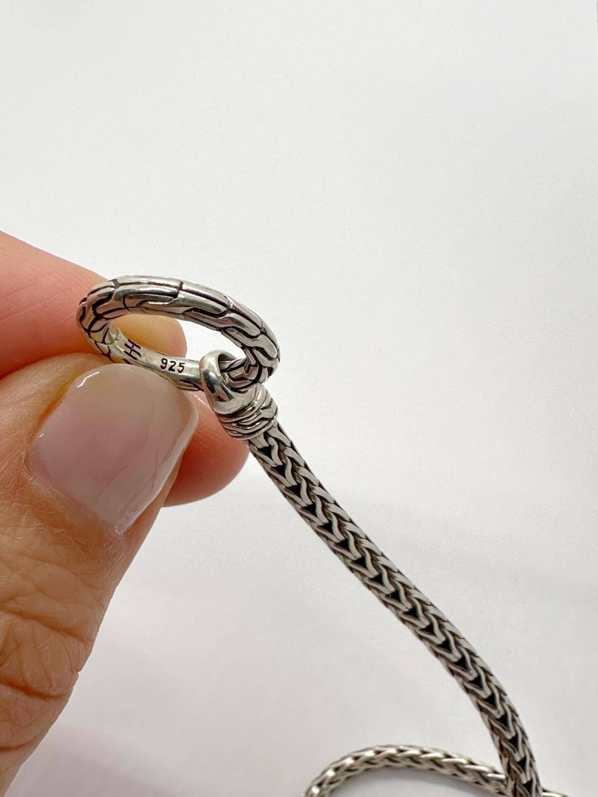 hand showing John Hardy stamp on silver necklace and white background