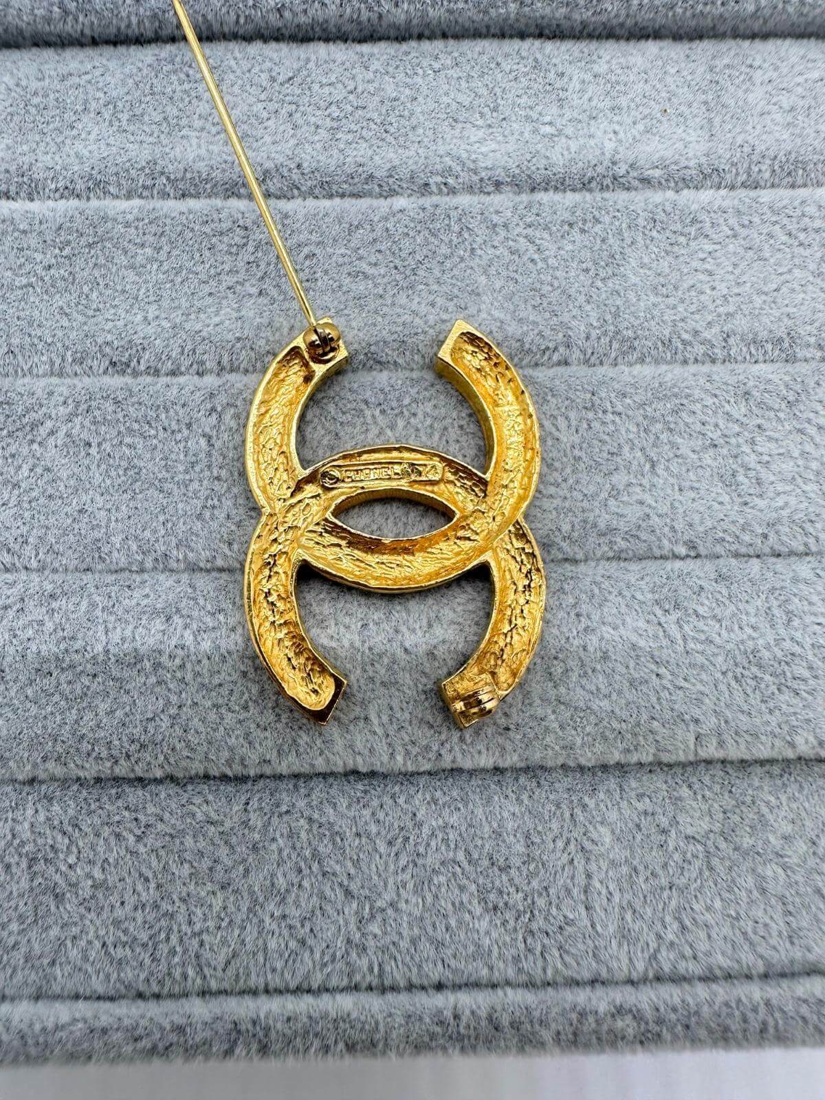 Pre-loved Chanel crystal brooch on grey background with signature