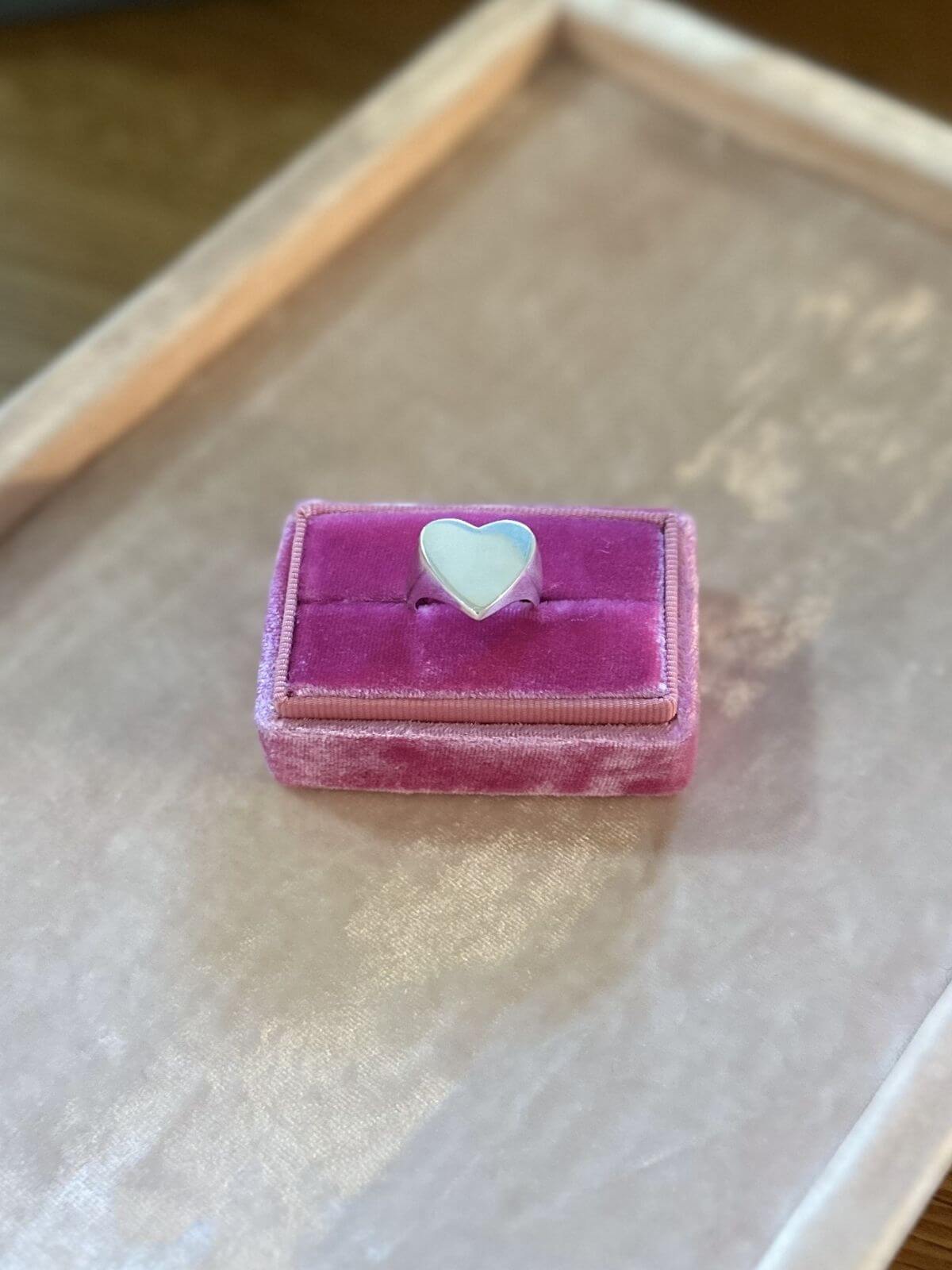 Pink velvet jewelry box with a heart-shaped object on a light wooden surface