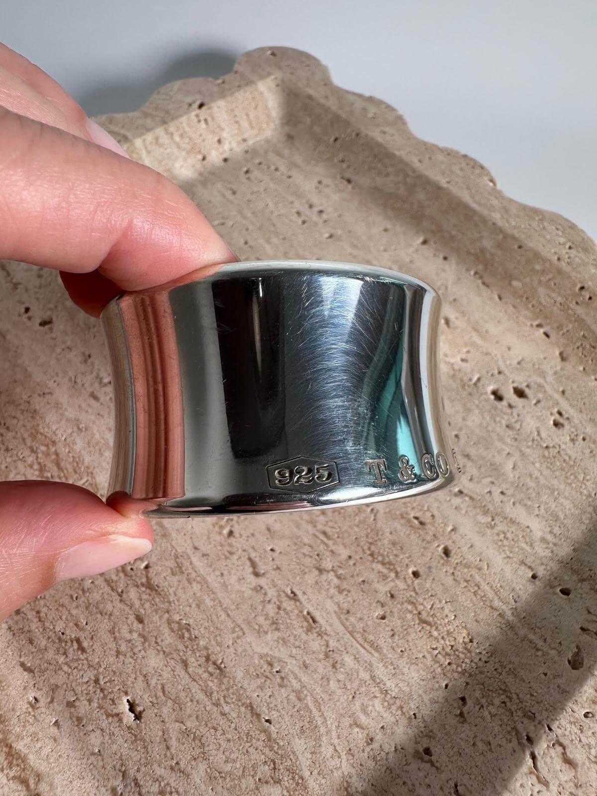 Silver cuff bracelet with 'T & Co' engraving on a marble background with hand