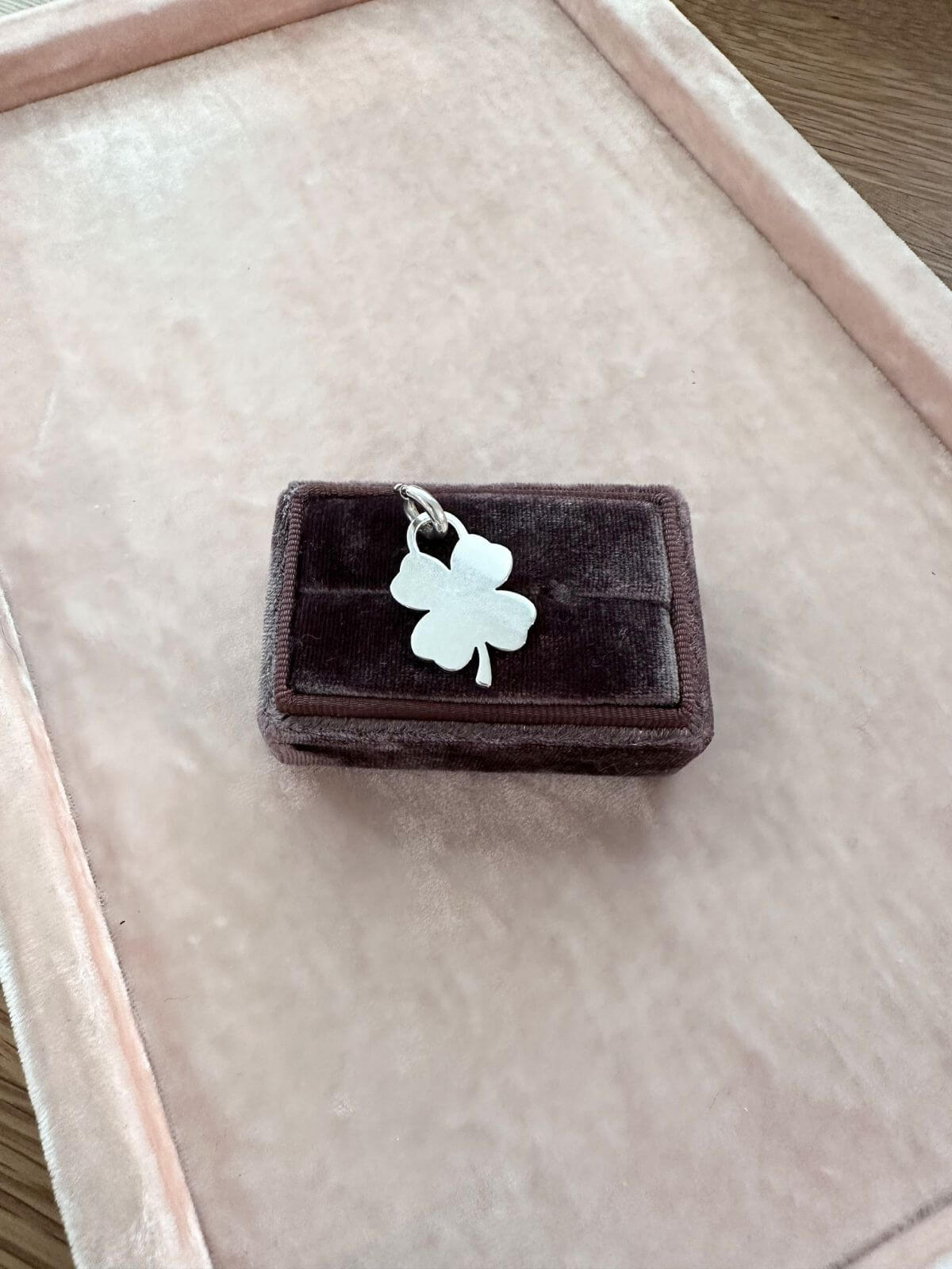 Tiffany & Co Silver four-leaf clover charm on a brown velvet box with a blurred background