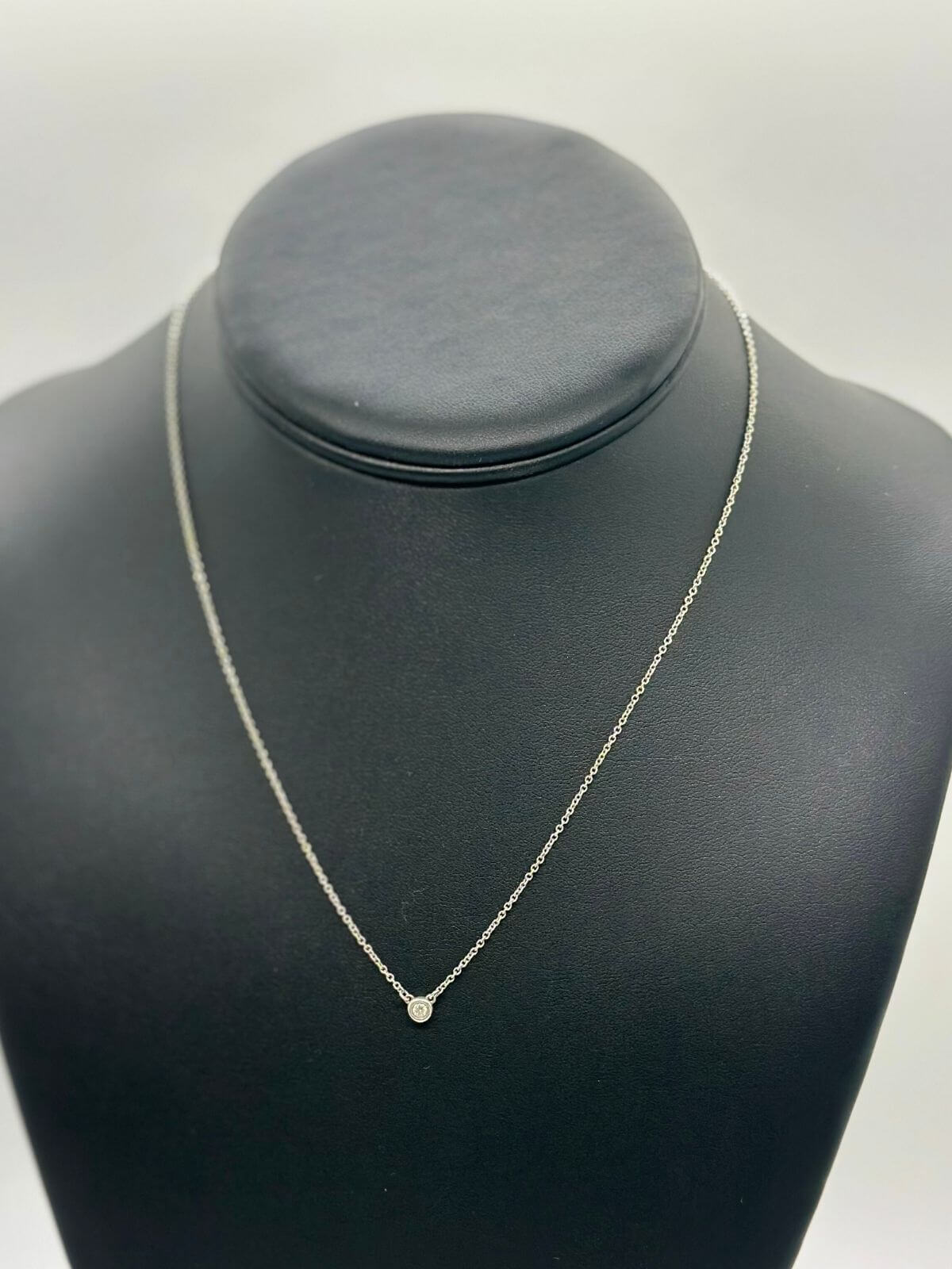 Silver Tiffany & Co solitaire diamond pendant on black fixture.