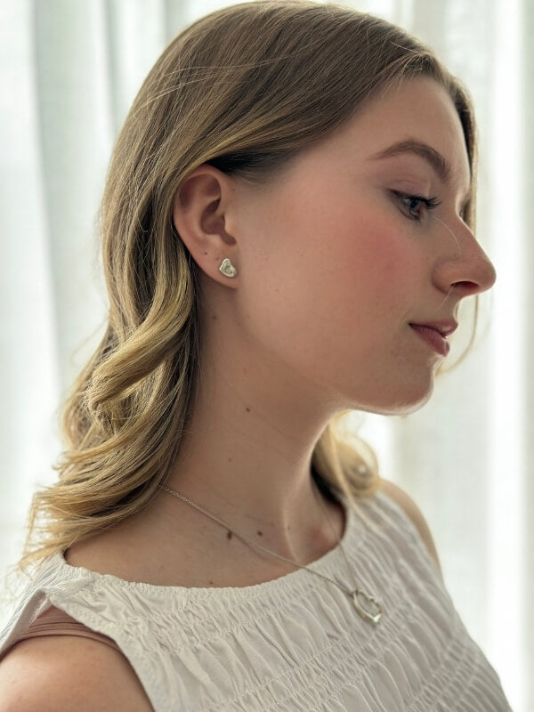 Louise Row Studio featuring TIffany Silver heart earrings on model in white top.