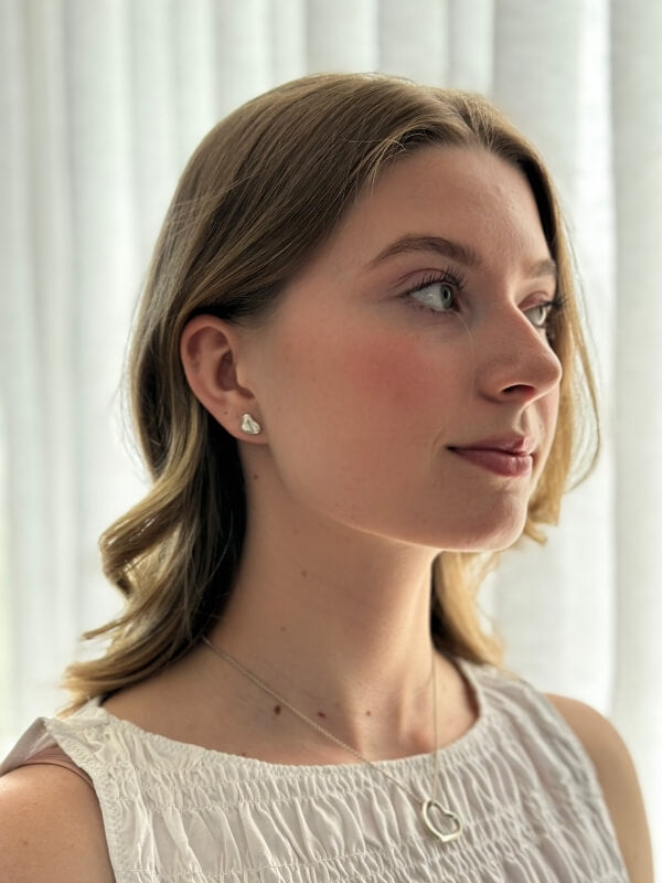 Louise Row Studio featuring TIffany Silver heart earrings on model in white top.