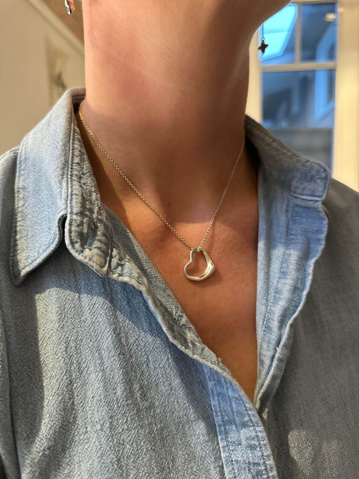 Heart-shaped necklace worn by a person with a denim shirt in the background
